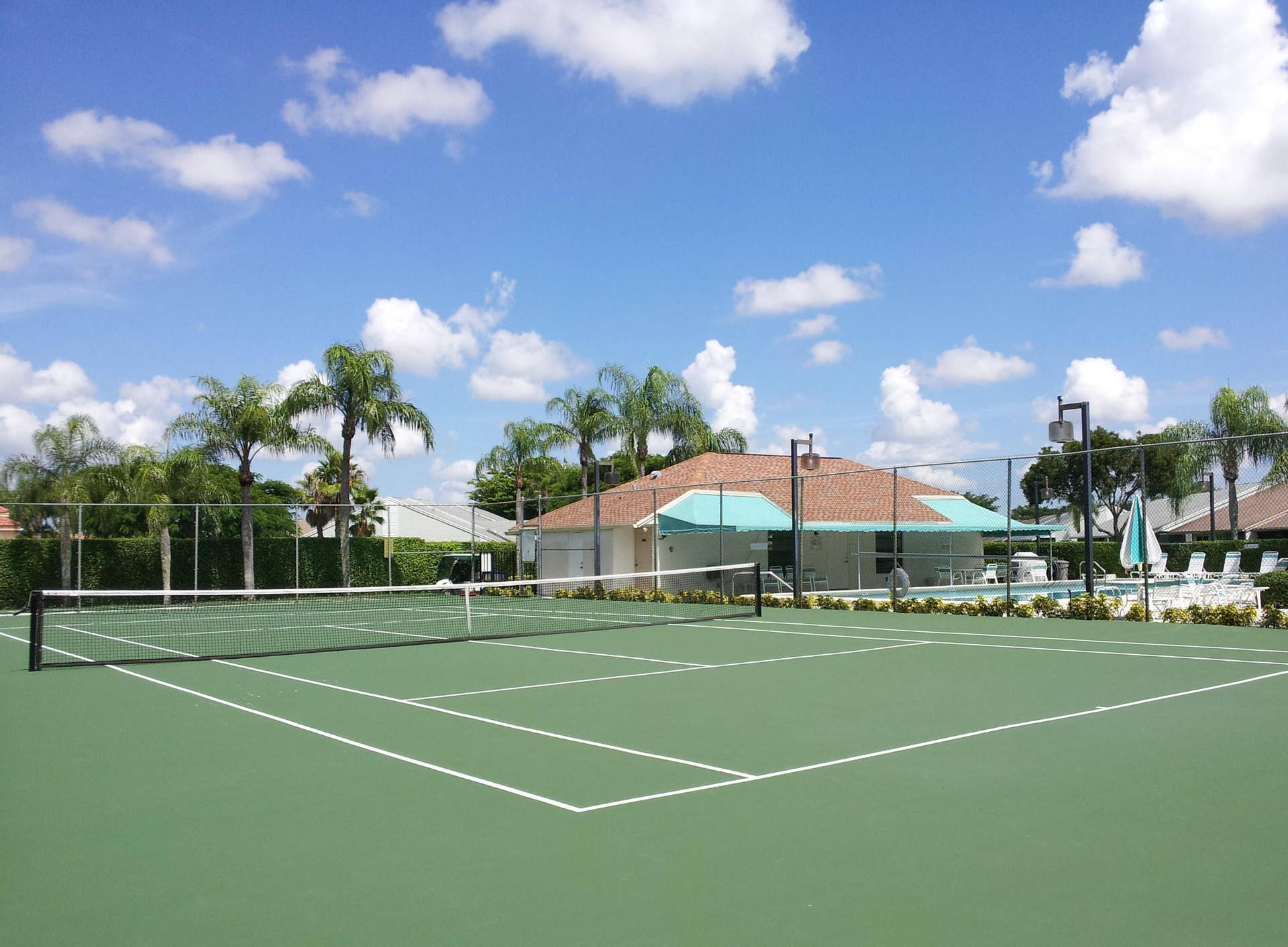 Tennis court with green surfacing, perimeter chain-link fencing, and pole-mounted exterior lighting