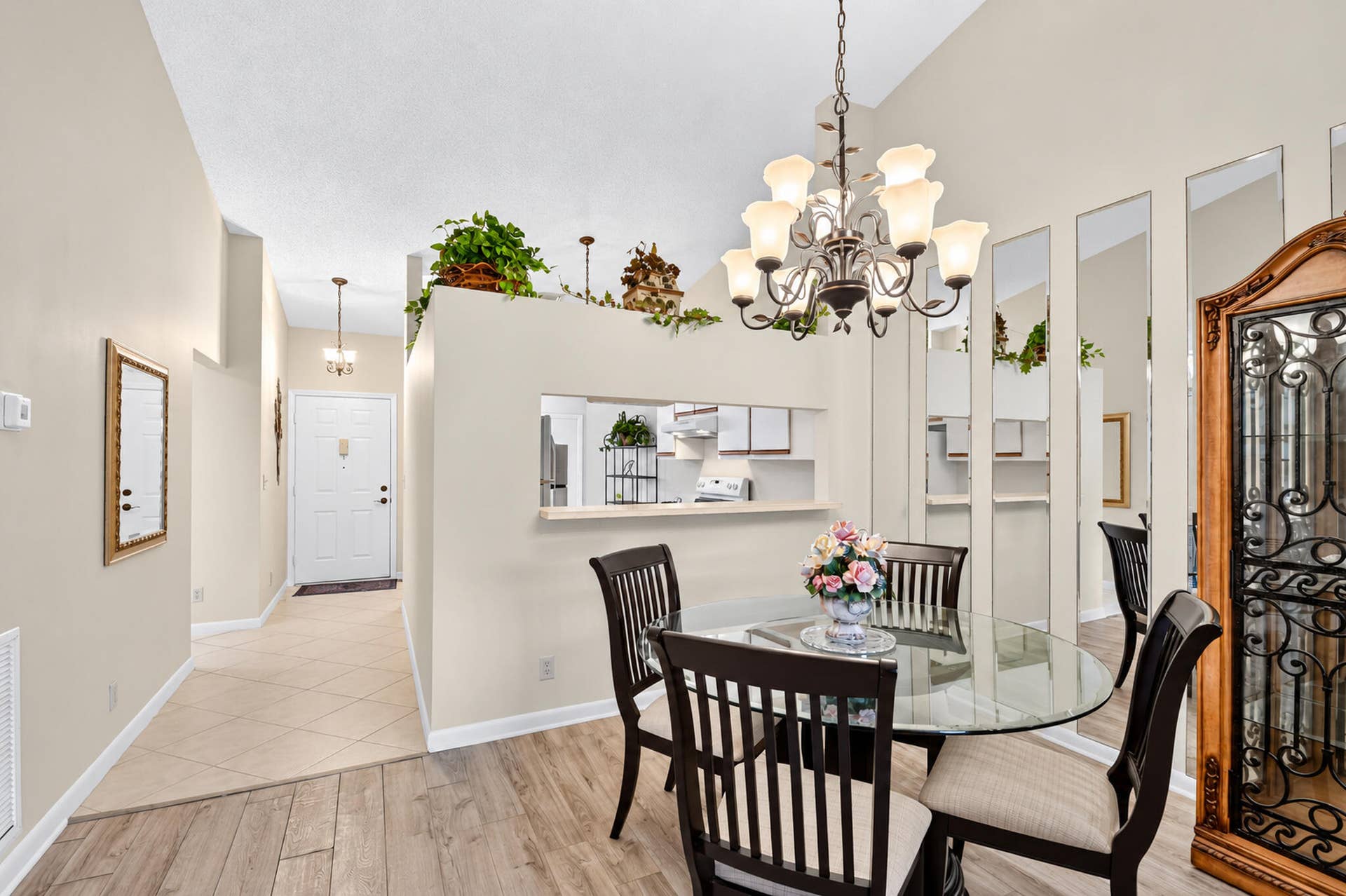 Vaulted ceilings, wood-finish flooring, decorative chandelier, pass-through wall opening, and floor-to-ceiling mirror paneling