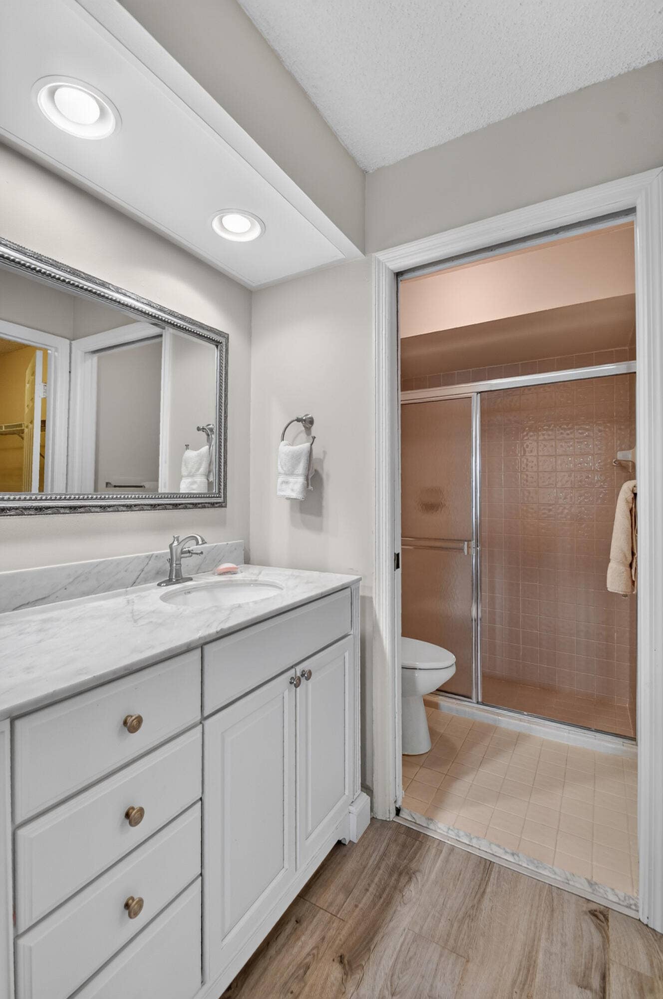 White vanity cabinet with an integrated stone-composite countertop, undermount sink, polished chrome faucet, framed mirror, and wood-finish flooring