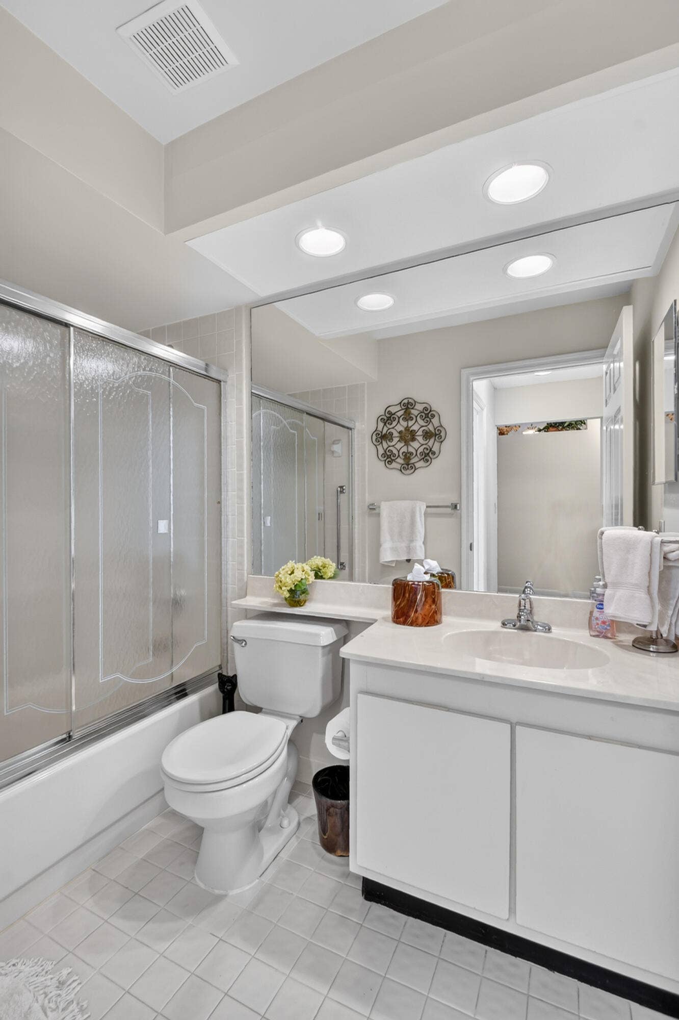 Bathroom featuring a white vanity with an integrated sink, large wall-mounted mirror, recessed lighting, and a tub-shower combination with sliding glass doors
