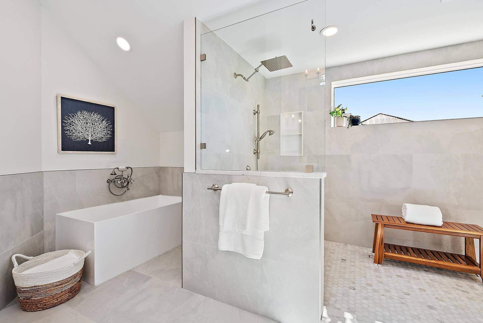 Freestanding rectangular soaking tub with wall-mounted faucet, walk-in shower with frameless glass enclosure, rainfall showerhead, and neutral large-format wall tile