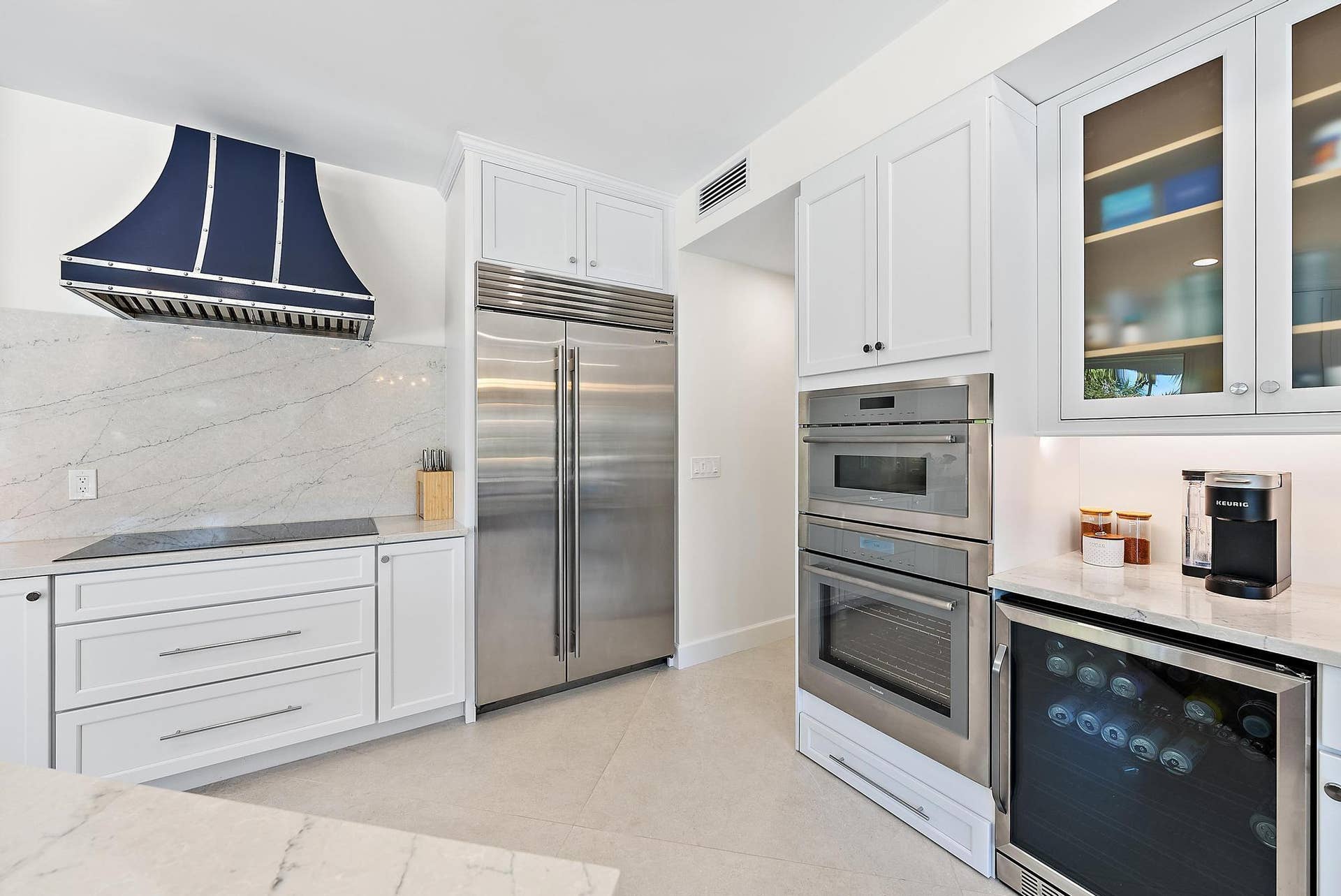 Kitchen featuring white cabinetry, custom range hood, integrated stainless steel refrigerator, built-in double wall ovens, and stone countertops
