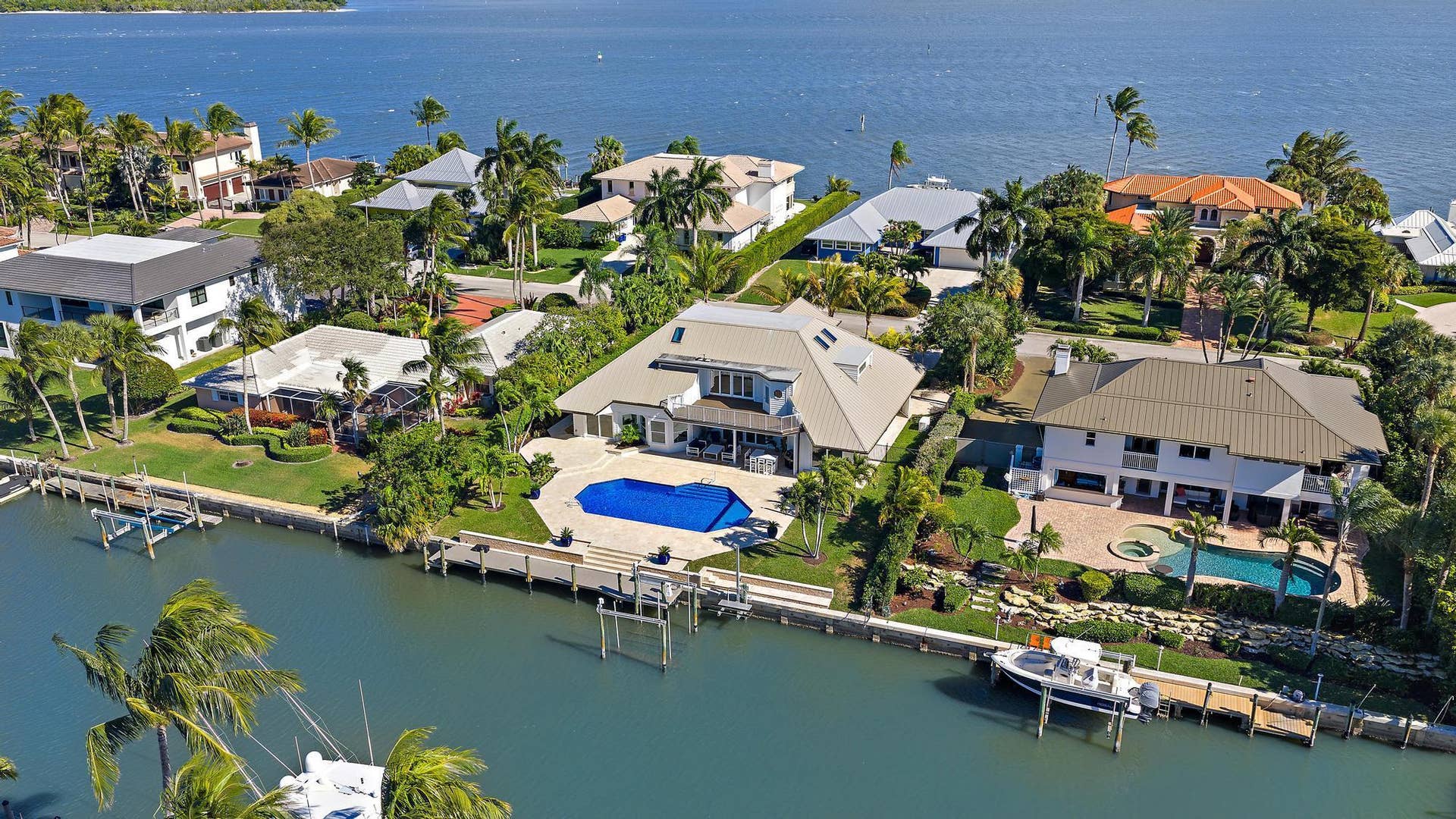 Waterfront property featuring a private boat dock, swimming pool, paved patio, and multi-level roofline