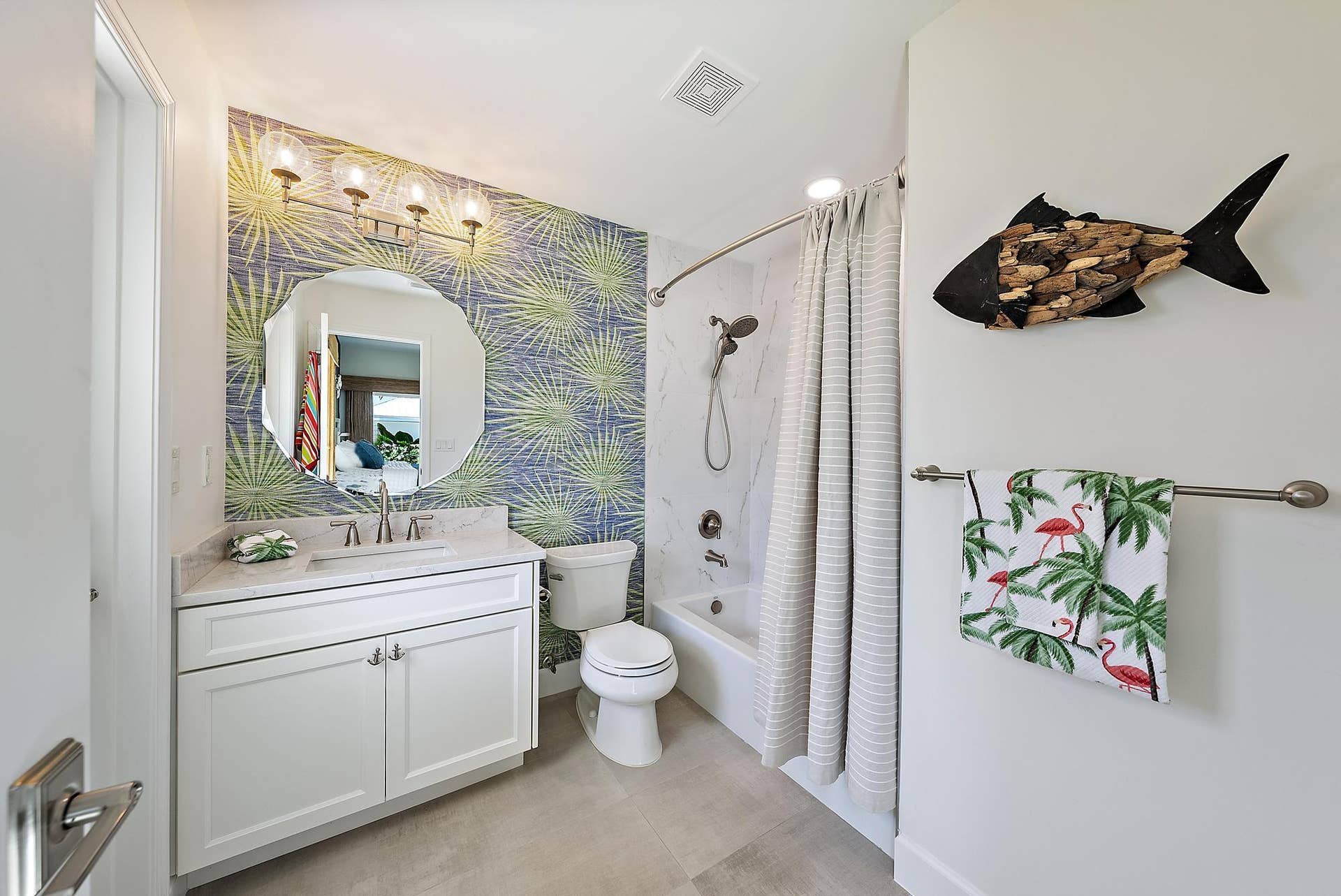 Bathroom featuring a white vanity cabinet with a stone-surface countertop, scalloped-edge wall mirror, four-light vanity fixture, and a tub-shower combination with full-height tile surrounds