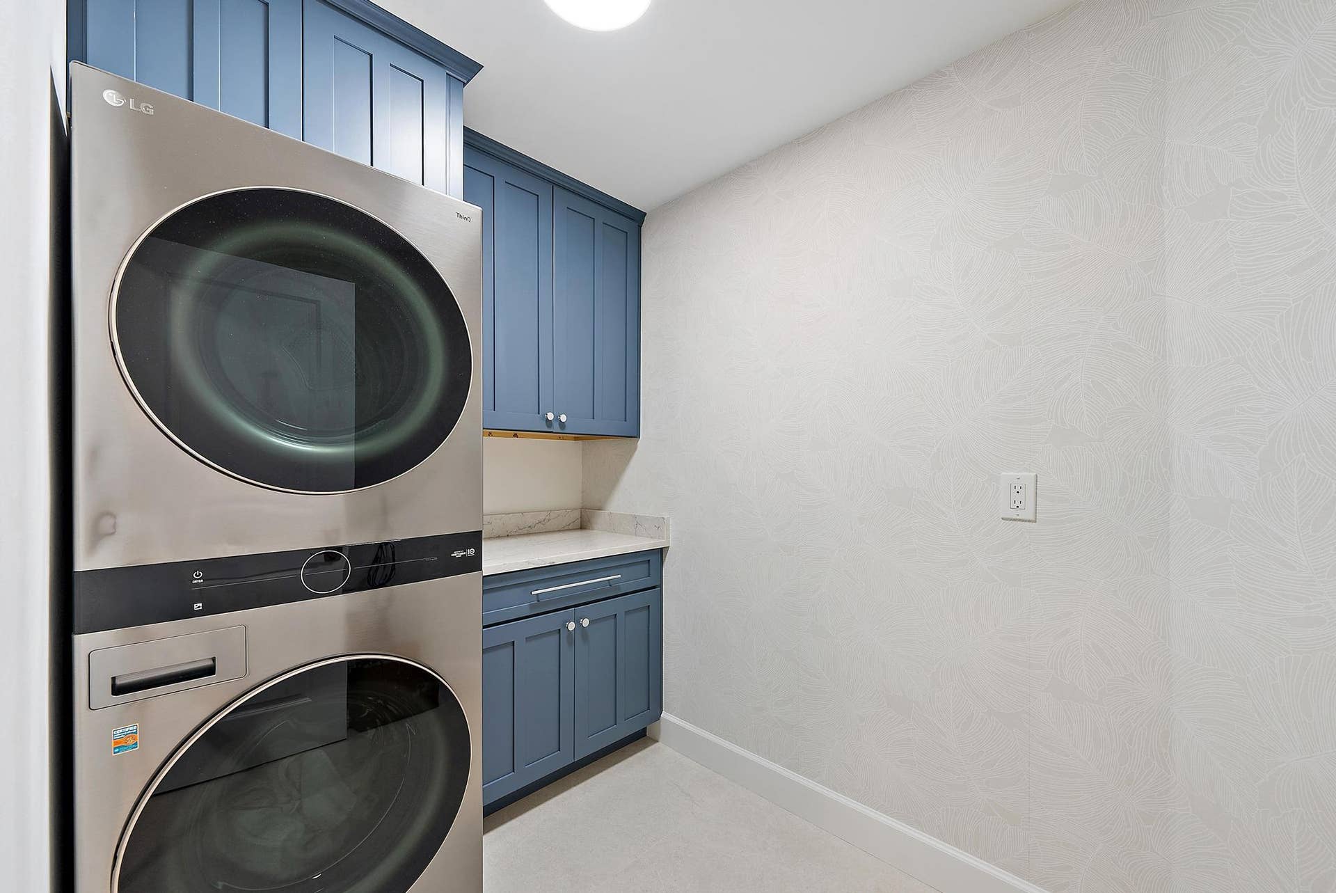 Laundry area featuring custom blue shaker-style cabinetry, stone-surface countertop, and stainless steel stacked appliance unit