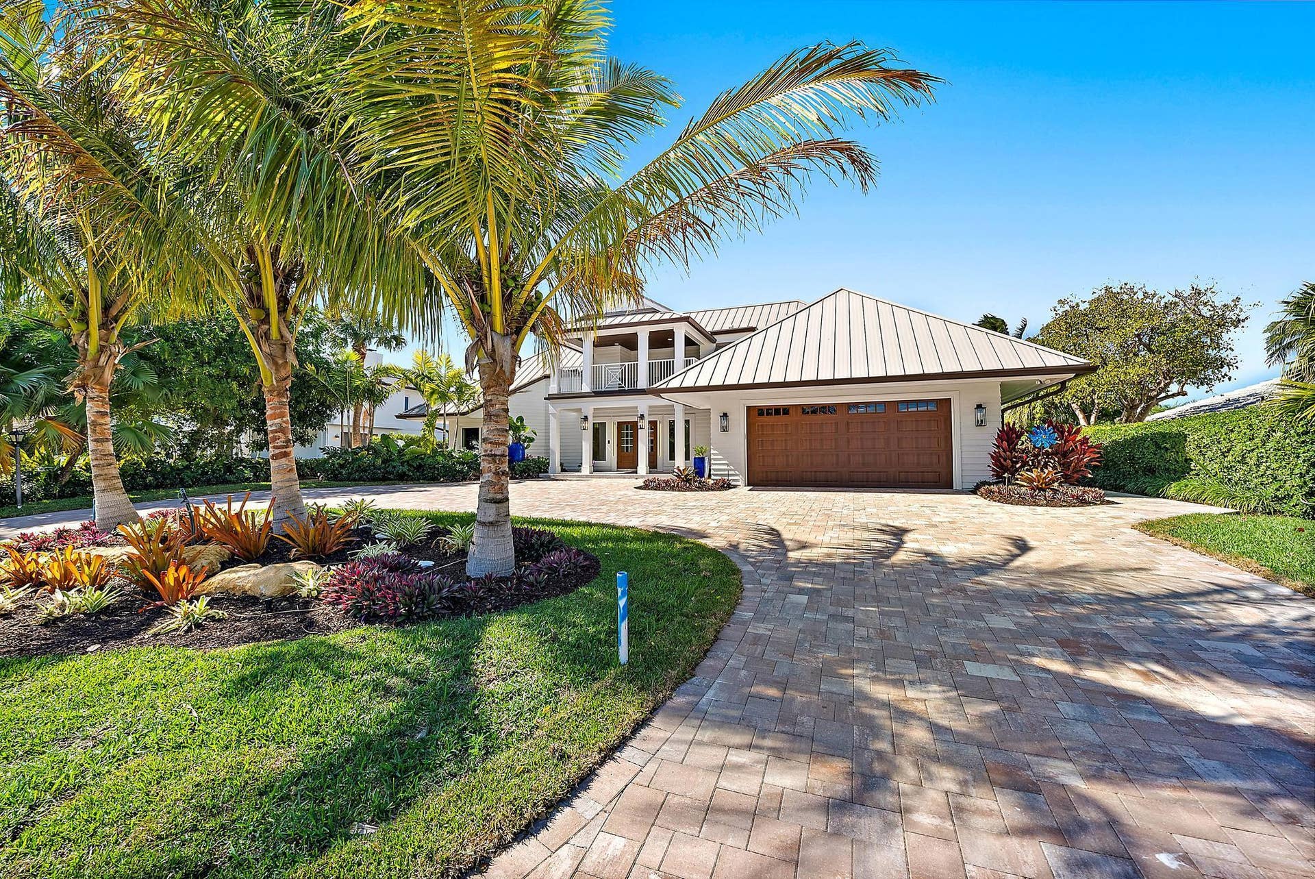 Exterior featuring a standing-seam metal roof, paver driveway, three-car garage, covered entry with a second-story balcony, and professional landscaping