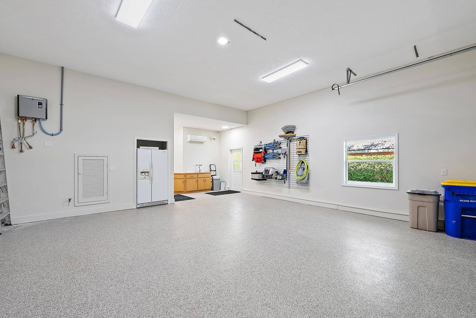 Garage interior featuring speckled epoxy flooring, built-in cabinetry, a wall-mounted ductless heating and cooling unit, overhead lighting, and a window