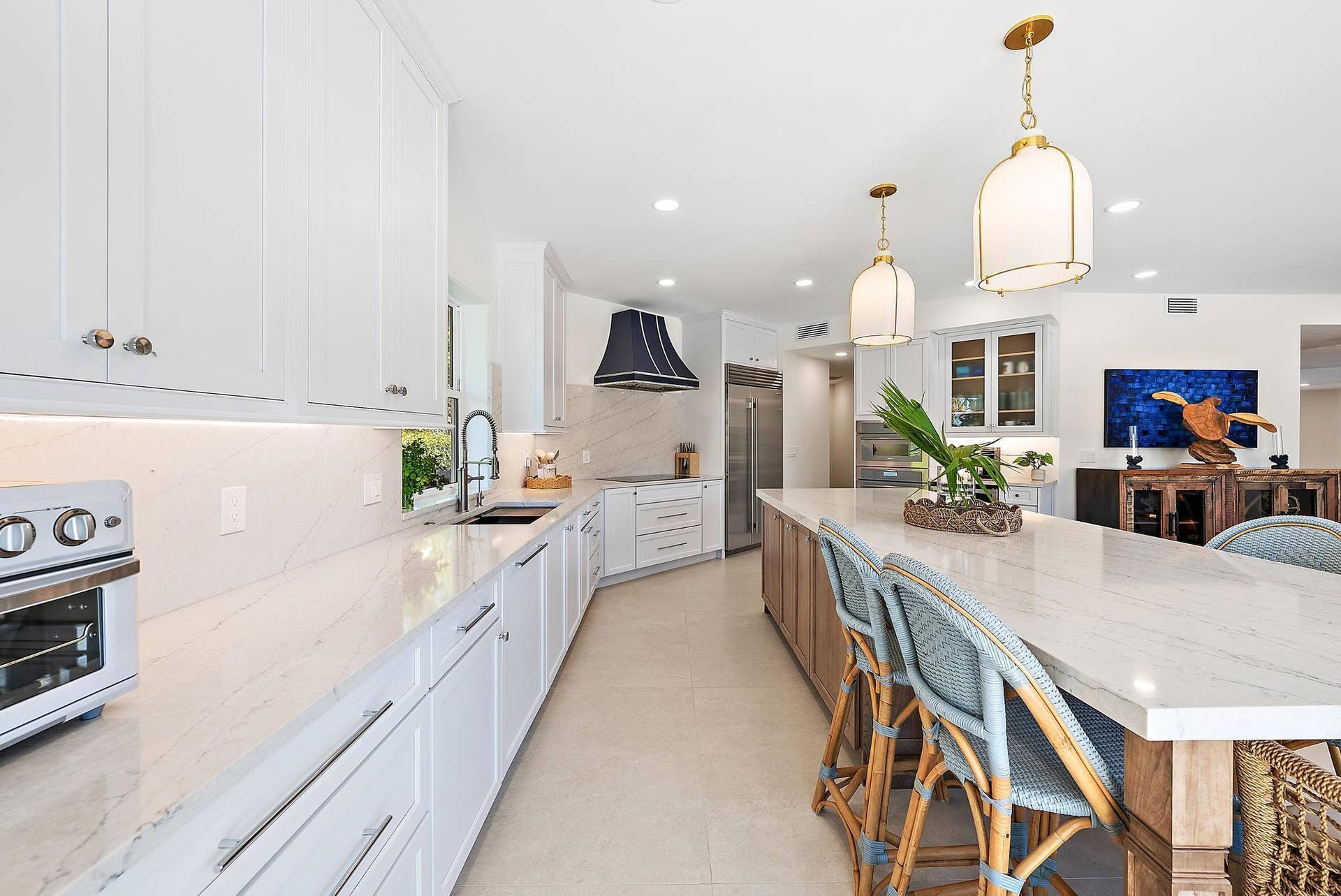 Kitchen featuring white shaker-style cabinetry, a large center island with stone-finish countertops, custom range hood, built-in stainless steel appliances, and pendant lighting