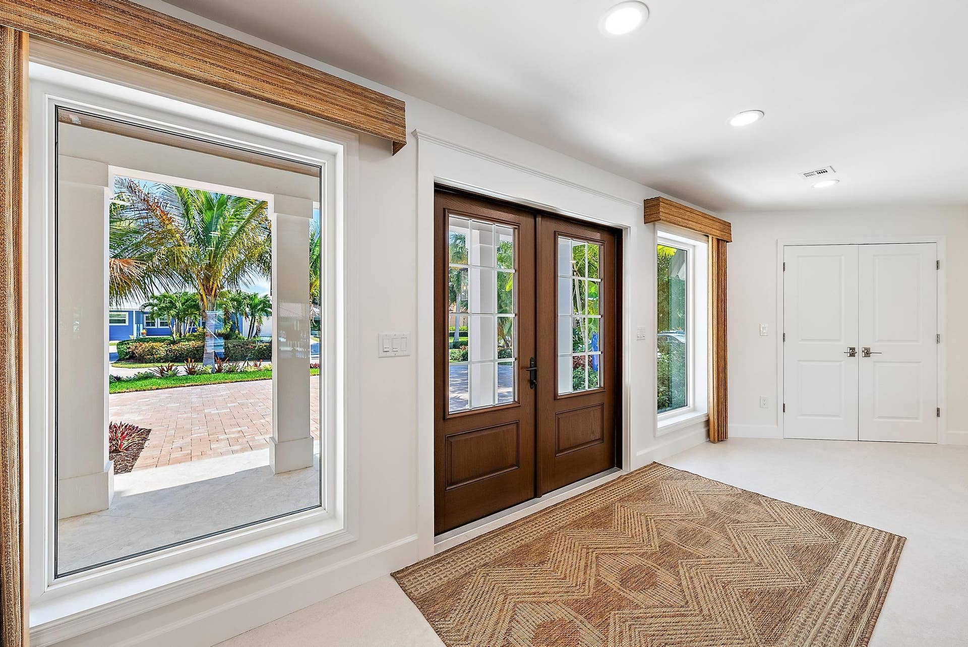 Double entry doors with divided-lite glass panels, neutral tile flooring, recessed ceiling lighting, and large picture windows featuring wood-finish valances