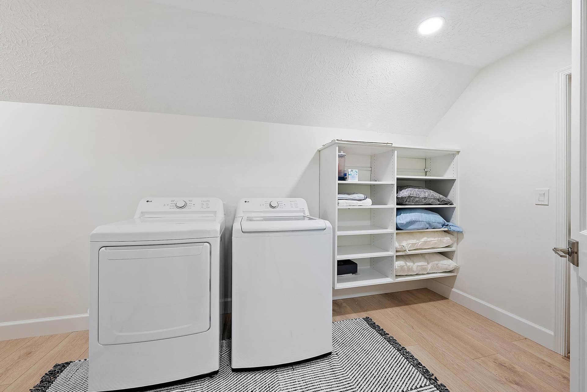 Dedicated laundry space featuring wood-finish flooring, recessed lighting, and wall-mounted white built-in shelving