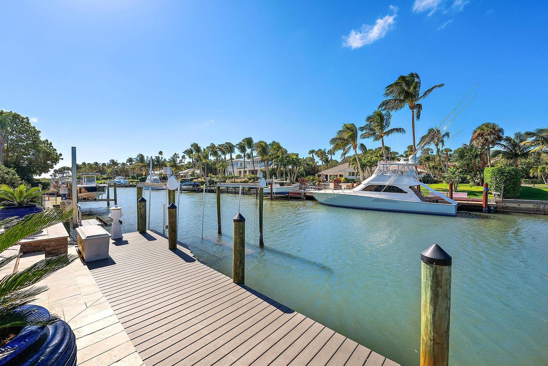 Waterfront property featuring a private boat dock, wooden decking, stone-tiled patio, and mature palm trees