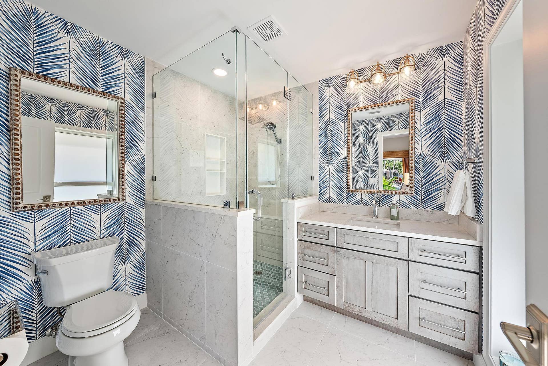 Bathroom featuring a glass-enclosed shower with stone-tile surround, custom wood-finish cabinetry, stone-top vanity, and dual wall-mounted mirrors with metallic trim