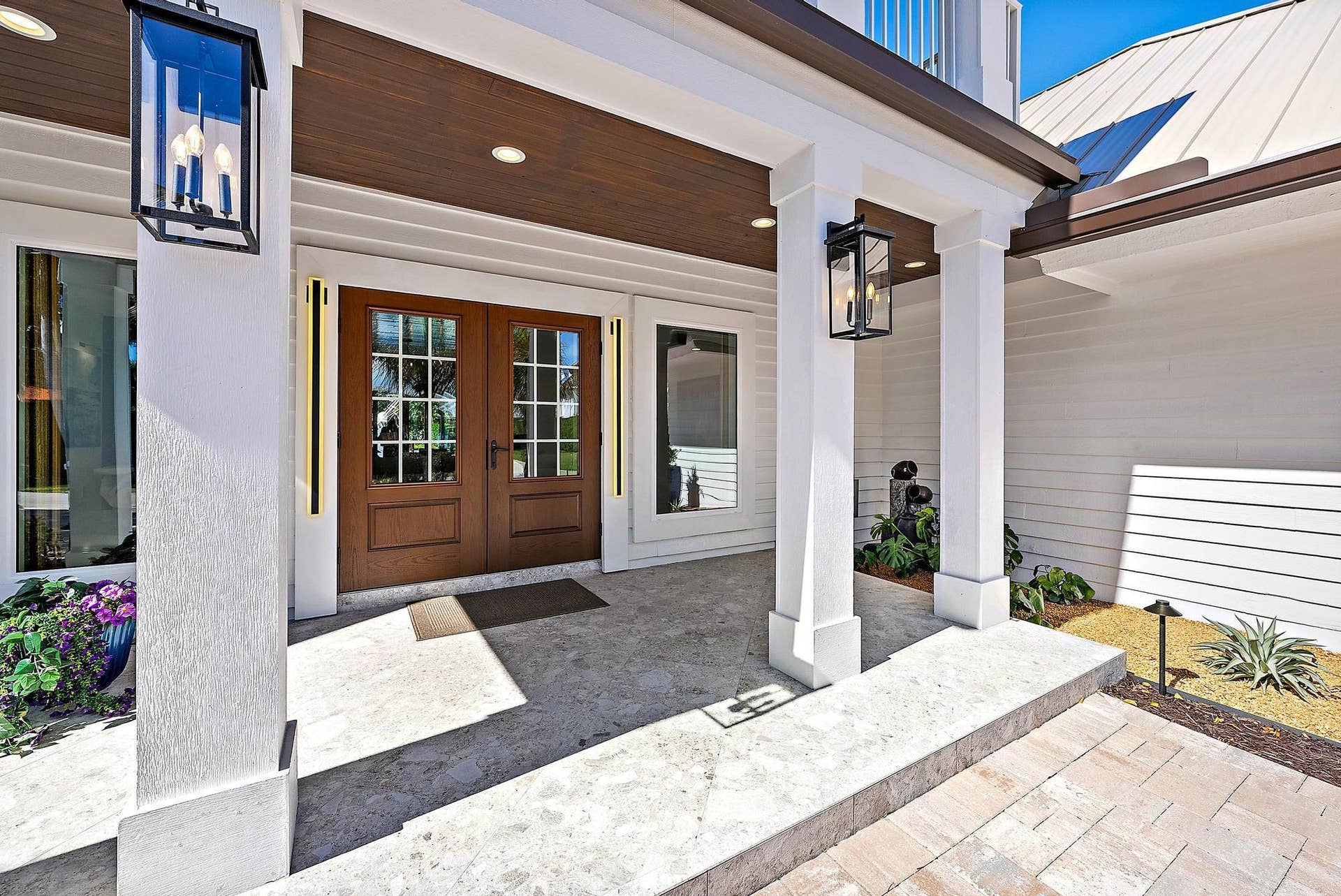 Covered entryway featuring horizontal lap siding, double wood-frame doors with glass panes, wood-finish ceiling cladding, stone flooring, and metal lantern-style wall sconces