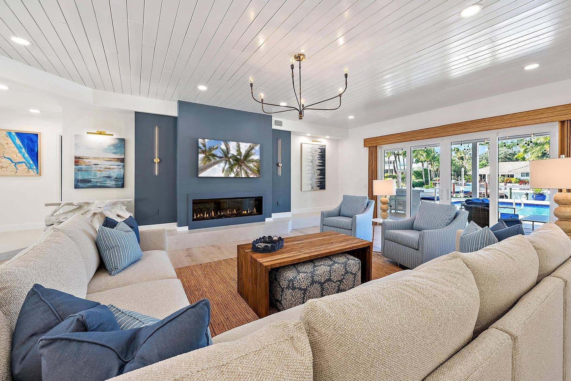 Spacious room featuring a white tongue-and-groove plank ceiling, recessed lighting, a modern linear fireplace with a blue accent wall, a minimalist black chandelier, and floor-to-ceiling glass sliding doors