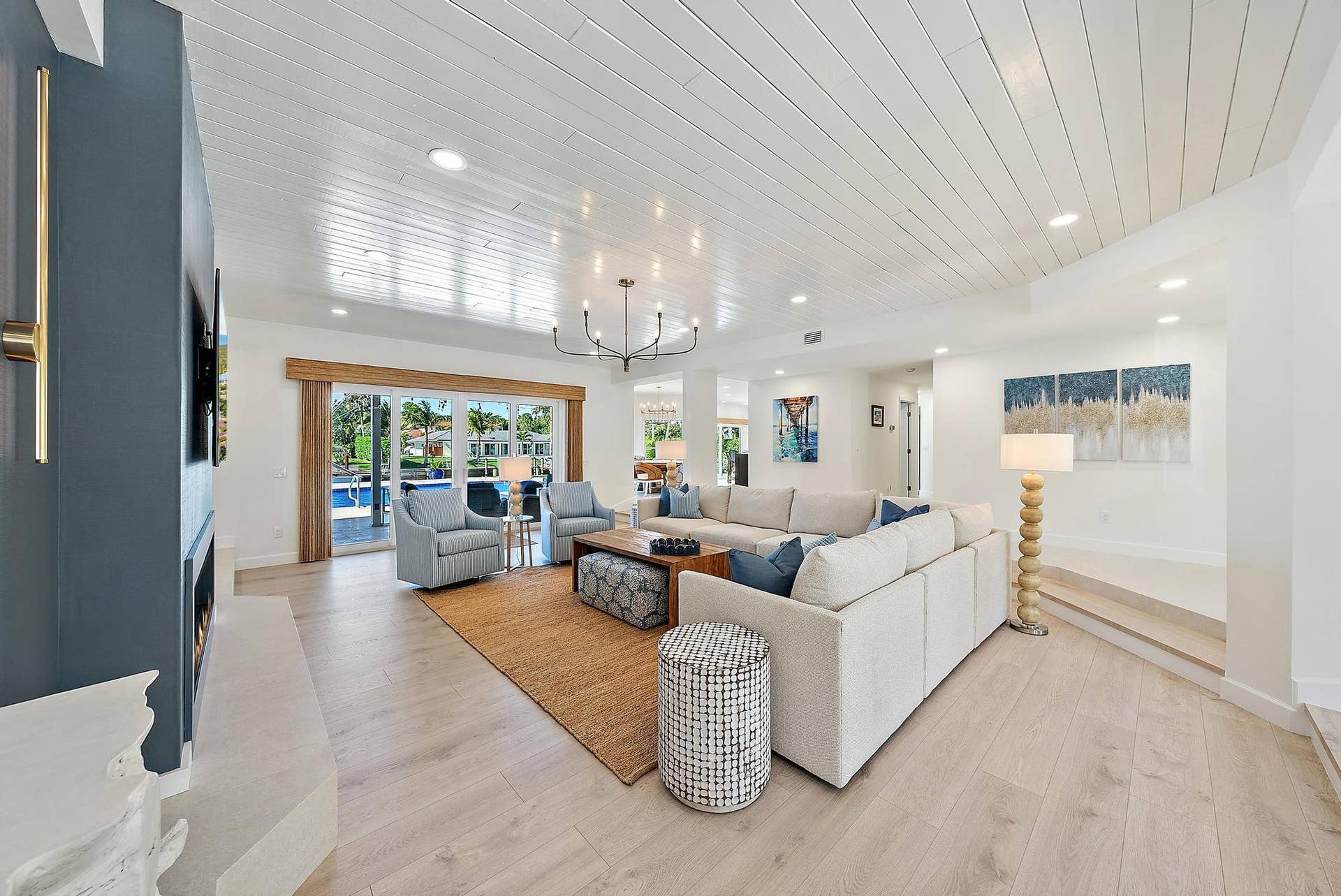 Living area featuring tongue-and-groove vaulted ceilings, wood-finish flooring, a linear fireplace with a floor-to-ceiling surround, recessed lighting, and large sliding glass doors