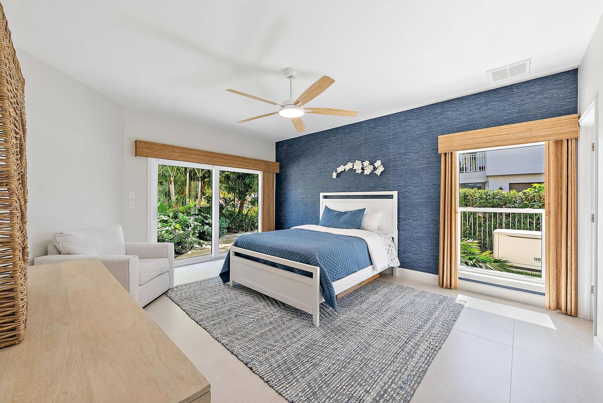 Textured navy blue accent wall, large-format tile flooring, ceiling fan with light fixture, and two sets of sliding glass doors featuring bamboo-finish window valances