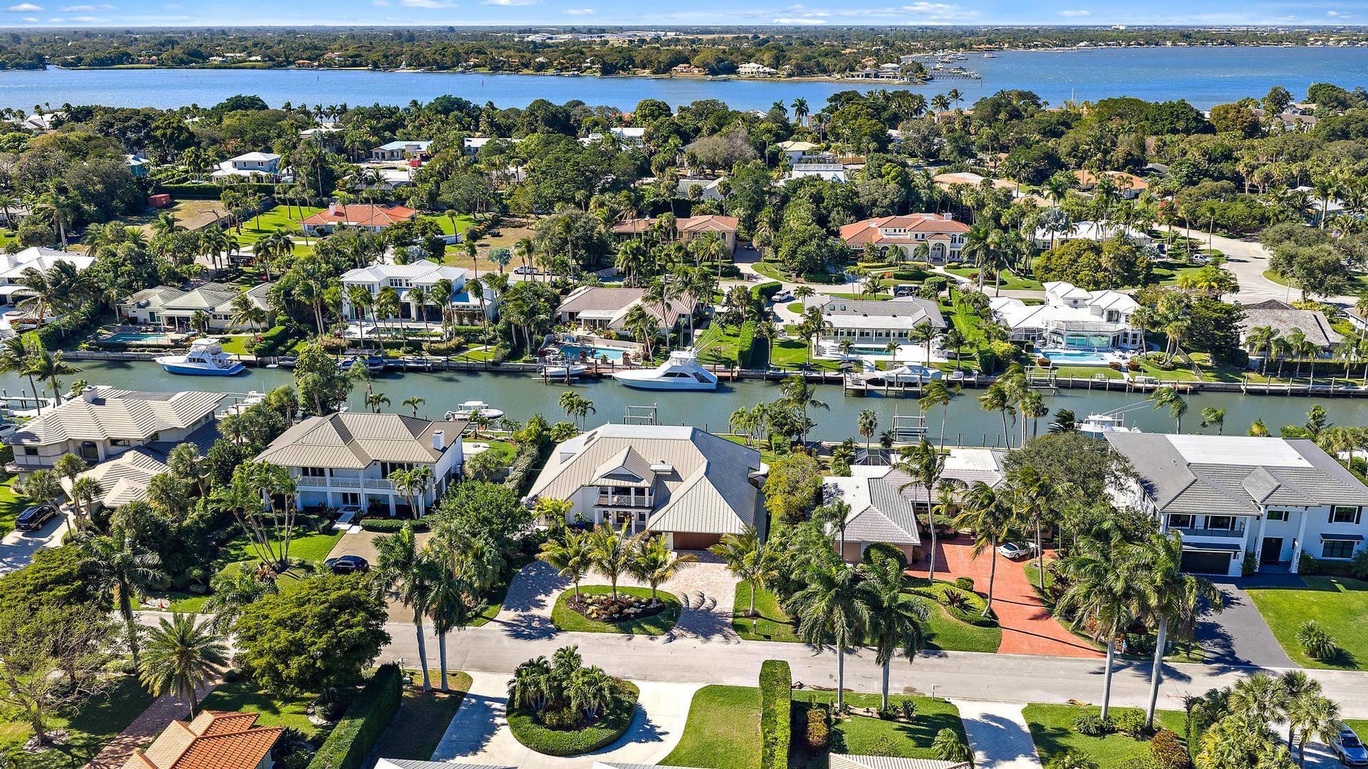 Aerial perspective of a waterfront community featuring deep-water canal access, private boat docks, paved driveways, manicured tropical landscaping, and mature palm trees