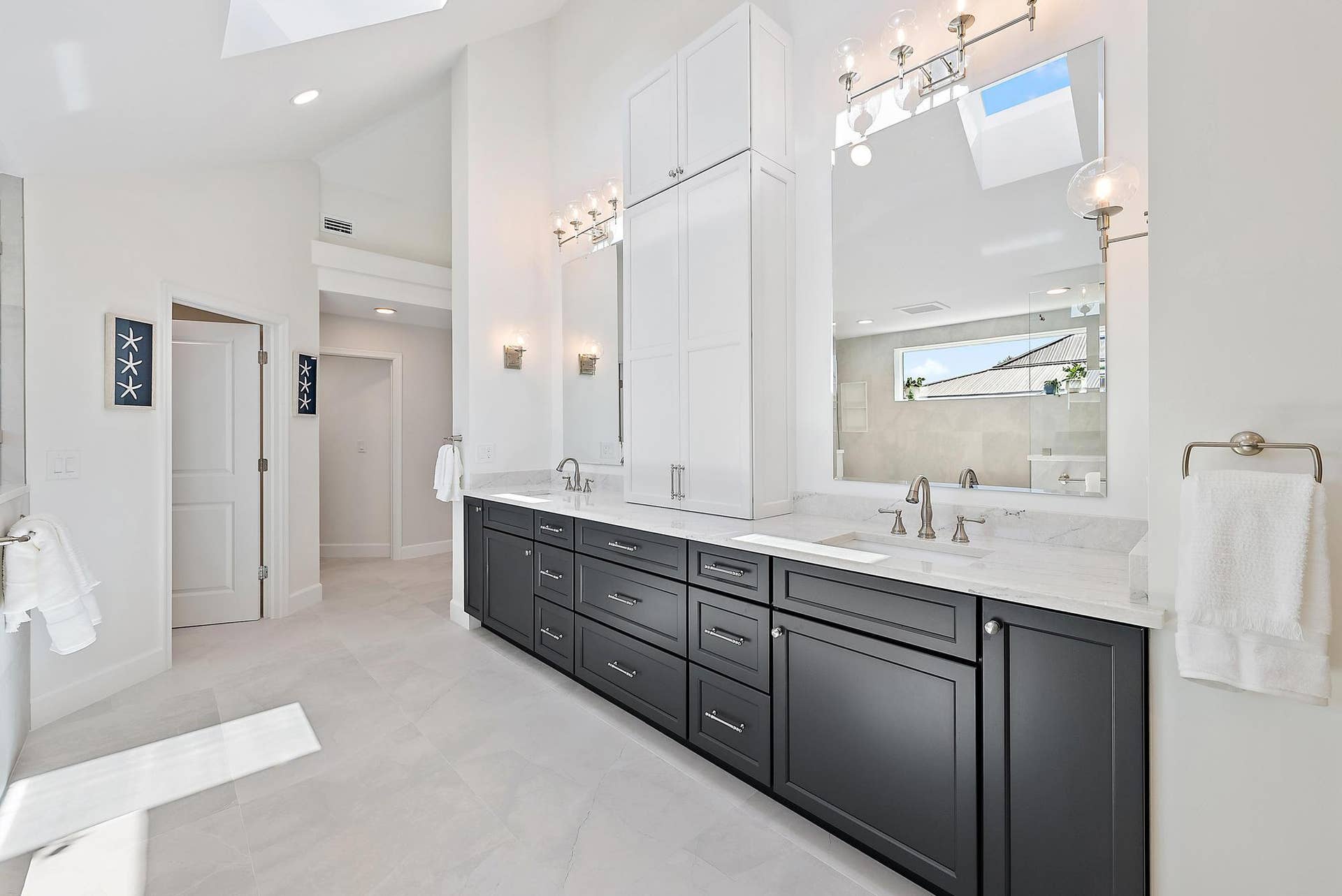 Dual-vanity bathroom featuring dark cabinetry, expansive stone countertops, integrated floor-to-ceiling storage, skylights, and polished metal fixtures
