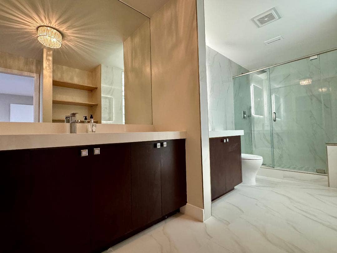 1127 BOCA COVE Lane, Highland Beach, FL 33487 Dual vanity with quartz vanities, dark wood-finish cabinetry, a large frameless mirror, and a crystal flush mount light fixture