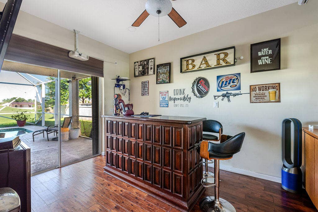 1233 Avondale Lane, West Palm Beach, FL 33409 Built-in wooden bar with paneled detailing, wood-finish flooring, ceiling fan, and sliding glass door access to a screened-in patio