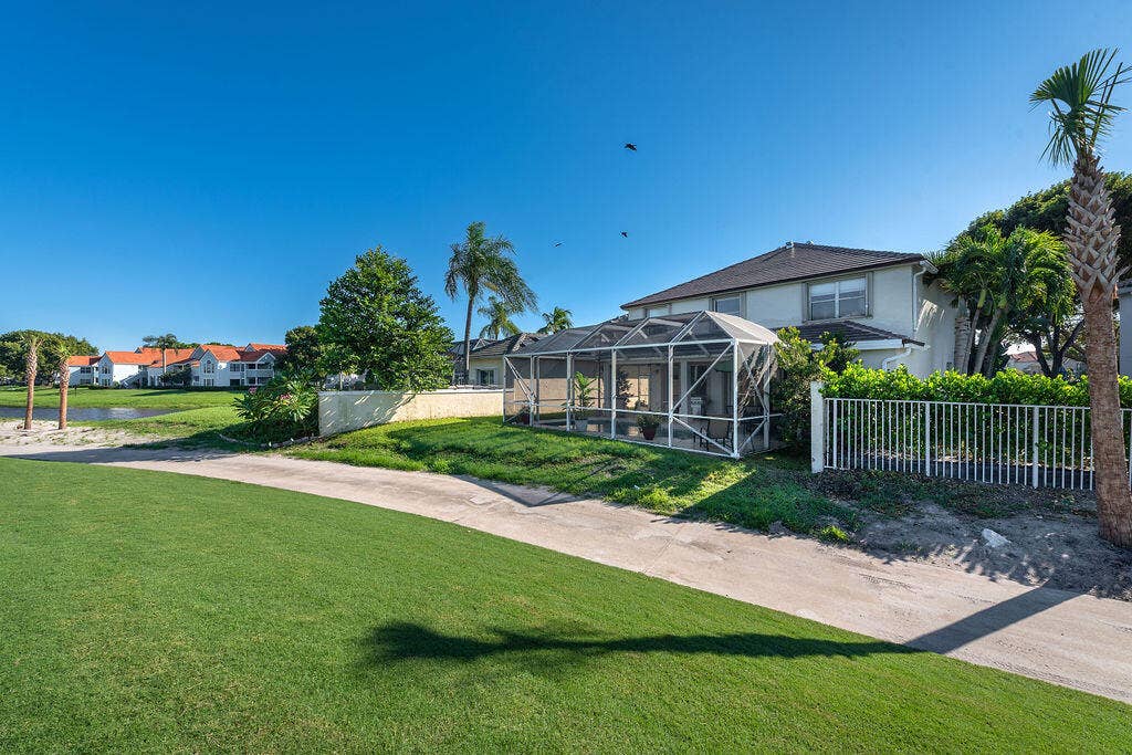 1233 Avondale Lane, West Palm Beach, FL 33409 Two-story residence featuring a screened-in lanai, concrete block exterior construction, a metal perimeter fence, and direct grass fairway frontage