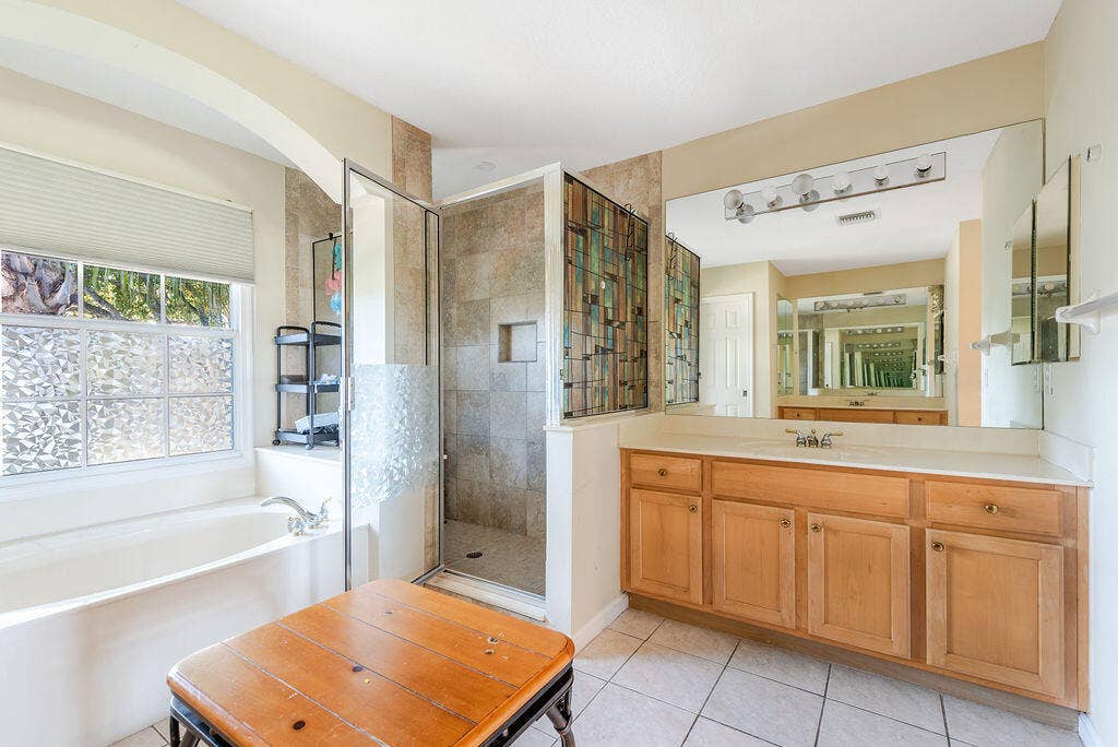1233 Avondale Lane, West Palm Beach, FL 33409 Bathroom featuring a deep soaking tub, separate walk-in shower with tile surround, wood-finish cabinetry, and a large vanity mirror with multi-bulb lighting