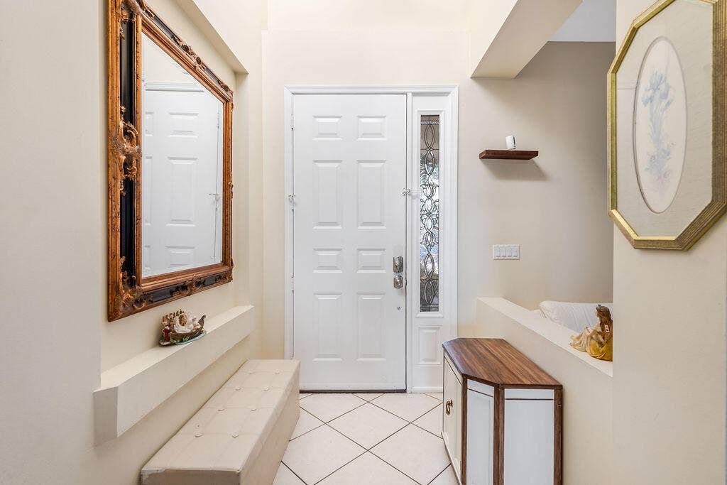 1233 Avondale Lane, West Palm Beach, FL 33409 Entryway featuring a panelled door with a decorative glass sidelight, tile flooring, and a built-in recessed display ledge