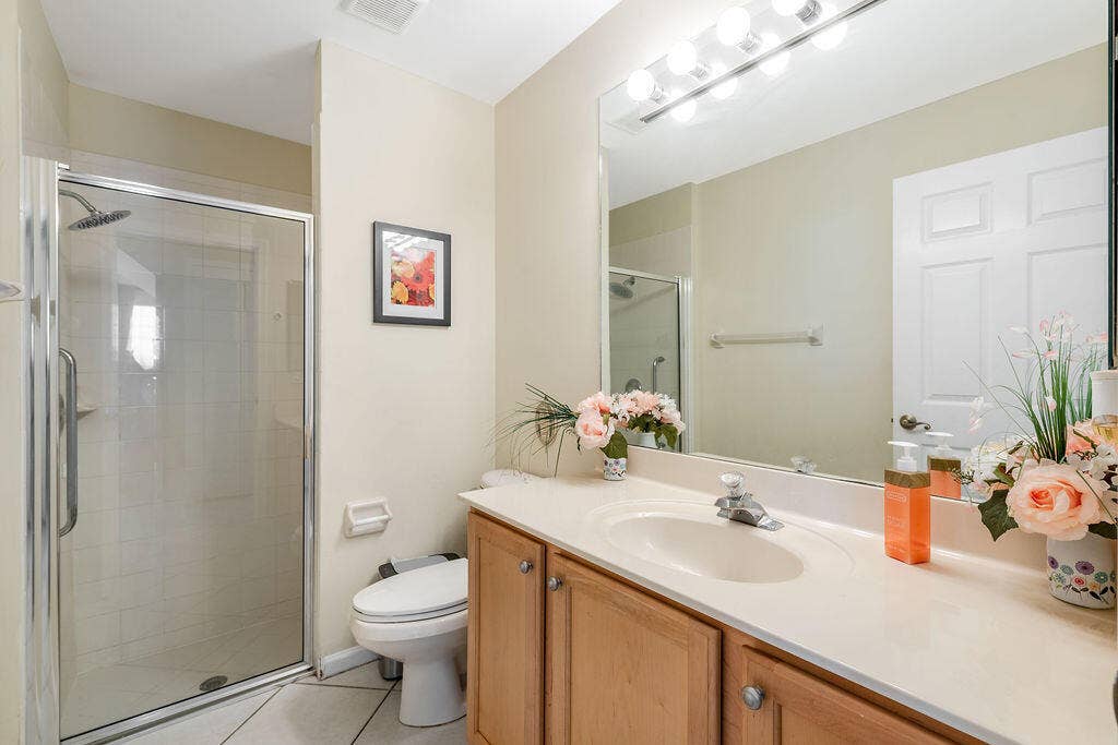 1233 Avondale Lane, West Palm Beach, FL 33409 Bathroom featuring a vanity with light-tone cabinetry and an integrated sink, a large wall-mounted mirror with integrated lighting, and a glass-enclosed shower with tile surround