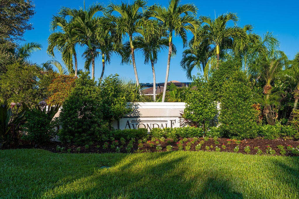 1233 Avondale Lane, West Palm Beach, FL 33409 Landscaped entrance featuring mature palm trees, manicured lawn, established shrubbery, and stone signage