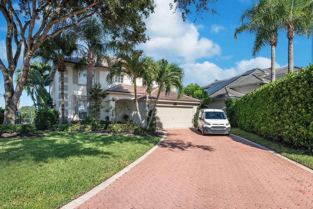 1233 Avondale Lane, West Palm Beach, FL 33409 Two-story residence featuring a paver driveway, an attached garage, and mature landscaping including palms and shade trees