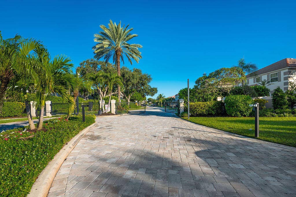 1233 Avondale Lane, West Palm Beach, FL 33409 Paver driveway entrance featuring mature palm trees, manicured landscaping, and wrought iron gate hardware
