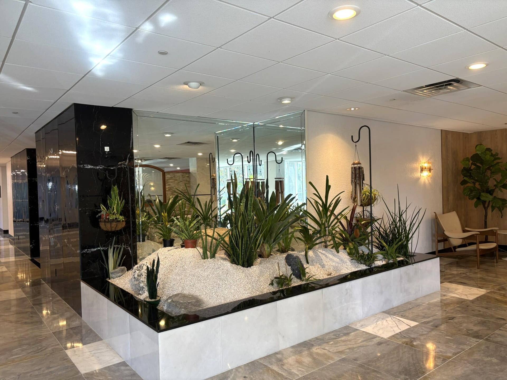 Interior garden feature with white stone bedding, polished black stone surround, mirrored wall panels, and recessed ceiling lighting