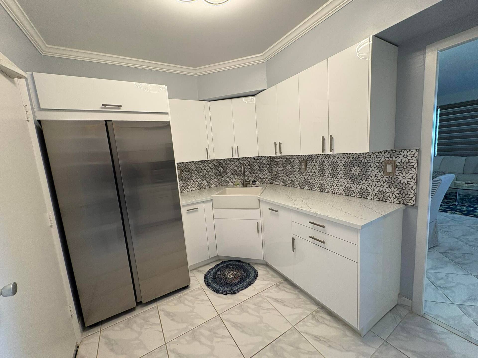 White cabinetry with metallic pulls, quartz countertops, patterned tile backsplash, stainless steel refrigerator, and apron-front sink
