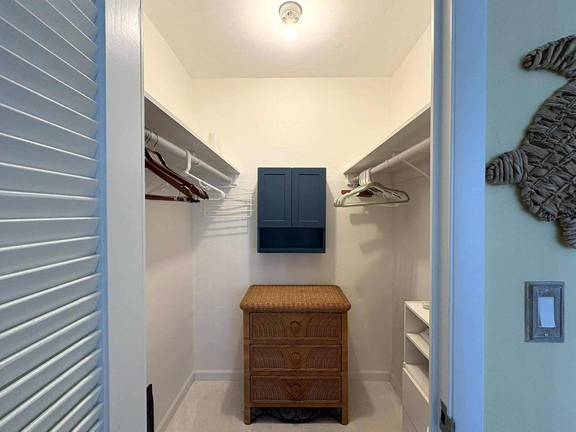 Walk-in closet featuring tiered shelving, dual hanging rods, and a wall-mounted navy blue storage cabinet