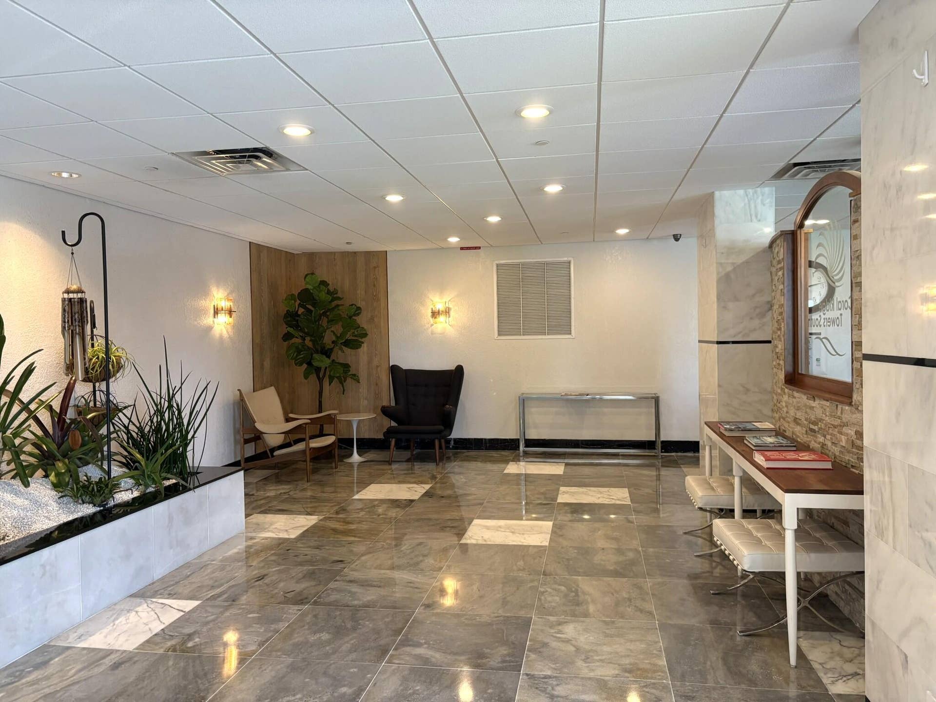 Lobby featuring polished stone flooring with inlaid tile accents, recessed lighting, wall-mounted sconces, and a built-in stone planter