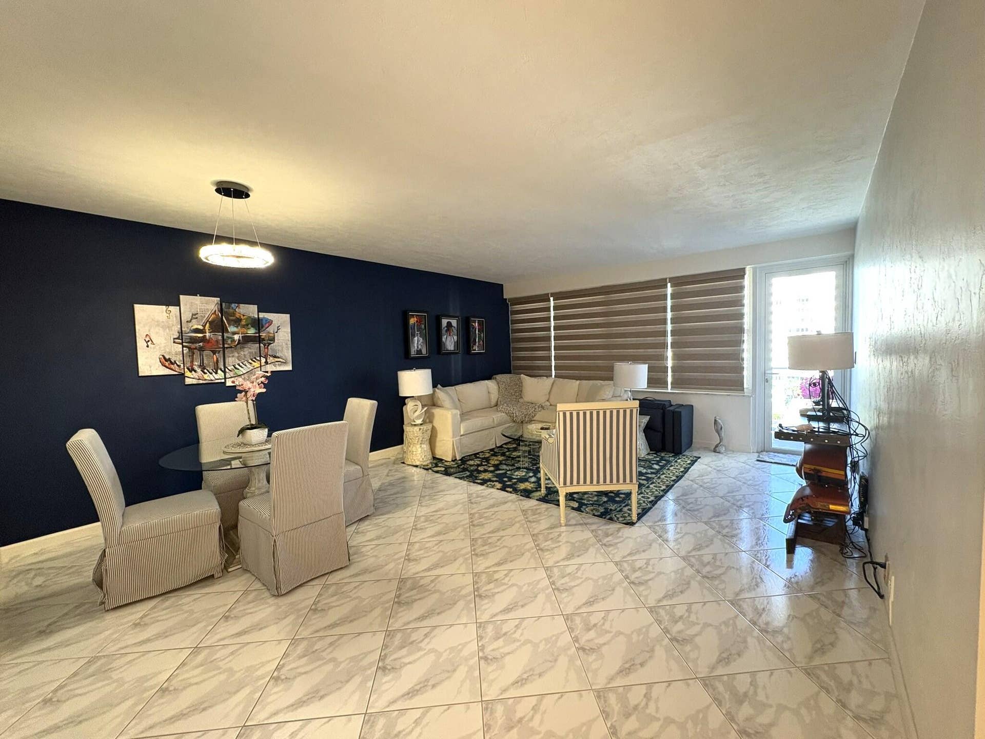 Open-concept area featuring stone-finish tile flooring laid on a diagonal, a modern ring-style pendant light fixture, and horizontal window shades