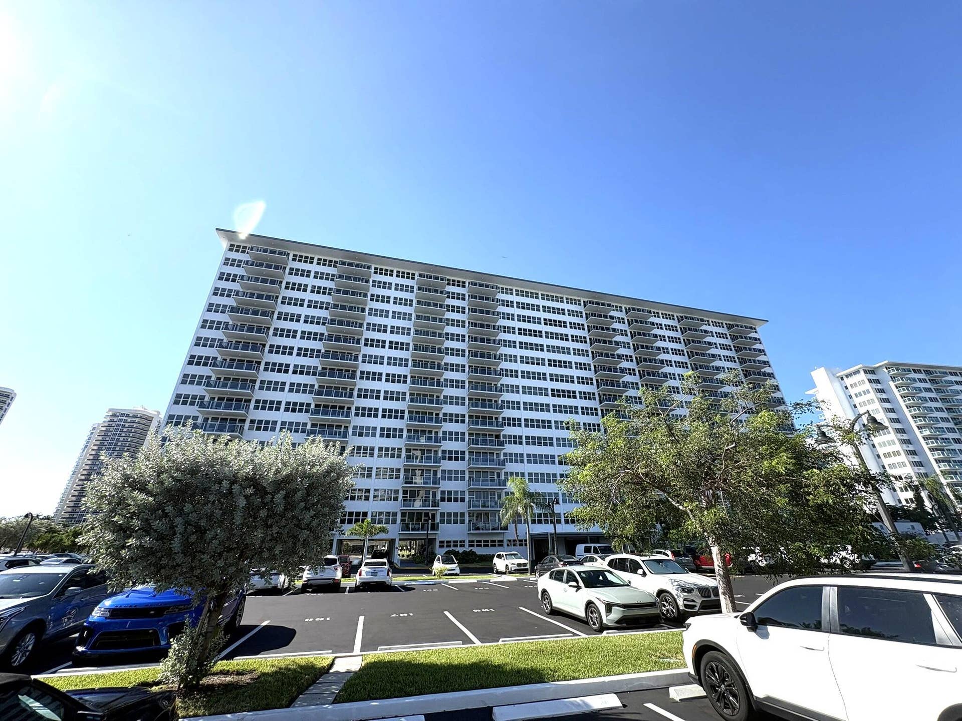 High-rise residential building featuring stacked private balconies, white exterior finish, and asphalt surface parking