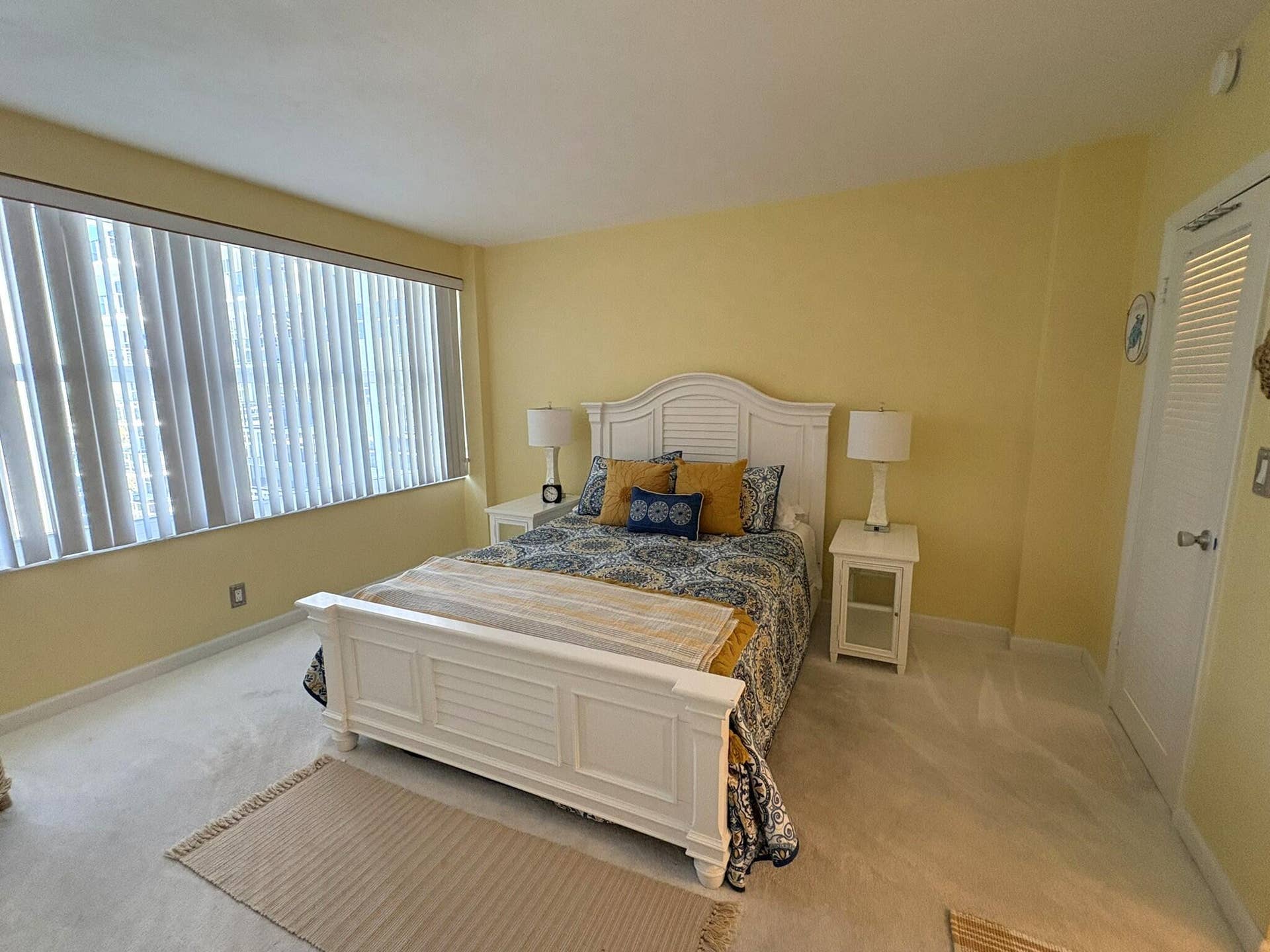 Room featuring wall-to-wall carpeting, large windows with vertical blinds, and a louvered-panel closet door