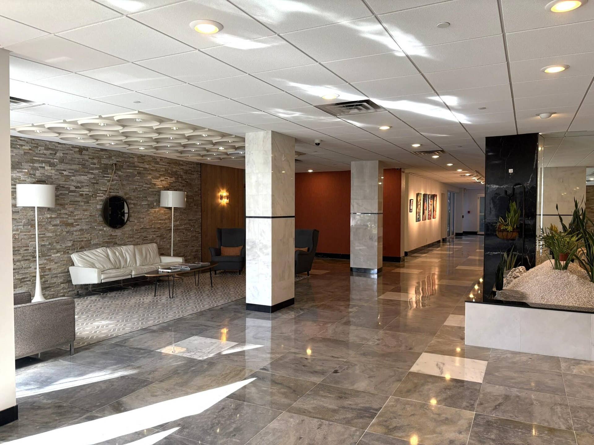 Lobby featuring large-format tile flooring, stacked stone wall cladding, polished structural columns, and recessed ceiling lighting