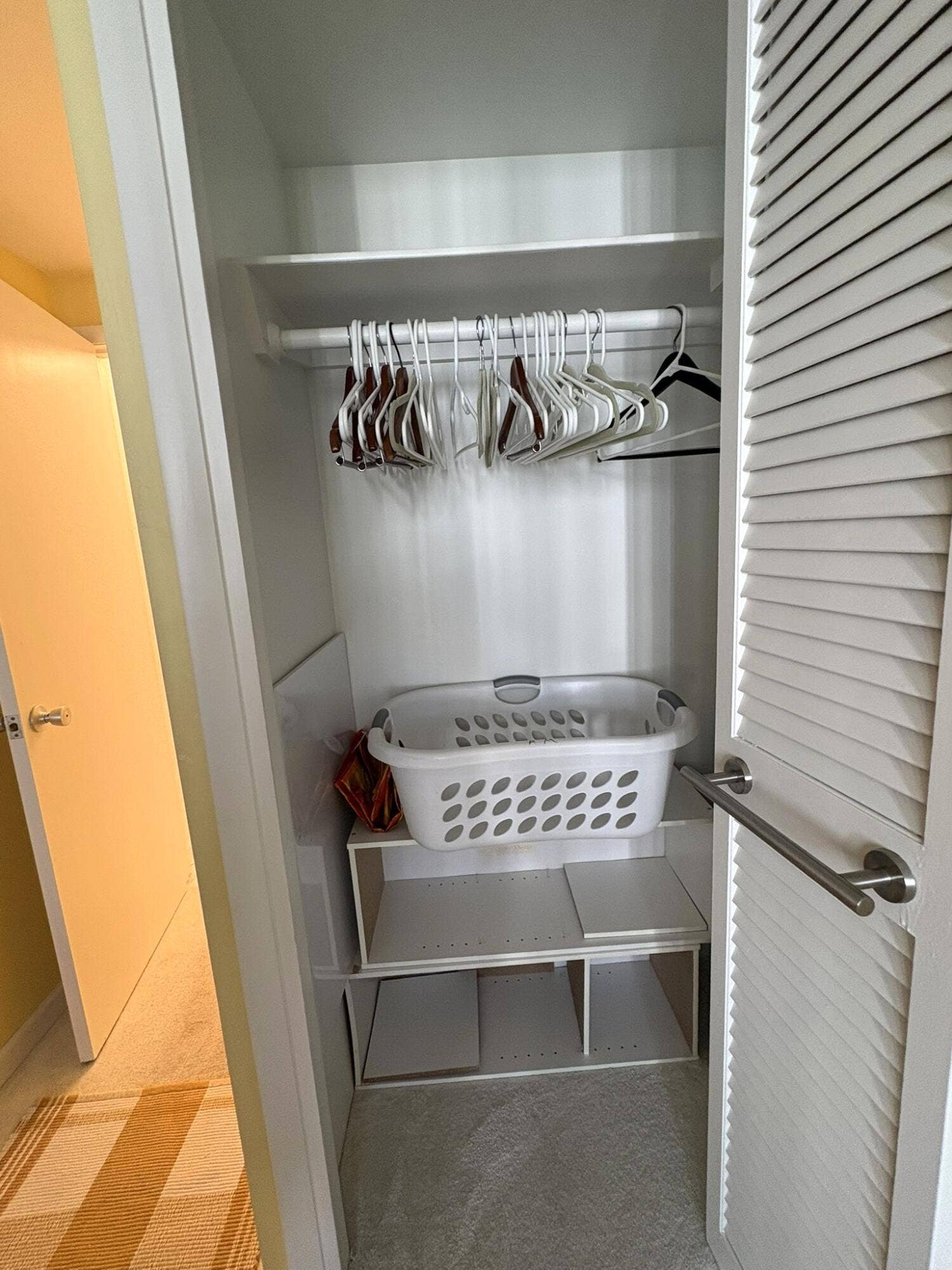 Closet featuring white louvered doors, built-in shelving, and a metal hanging rod
