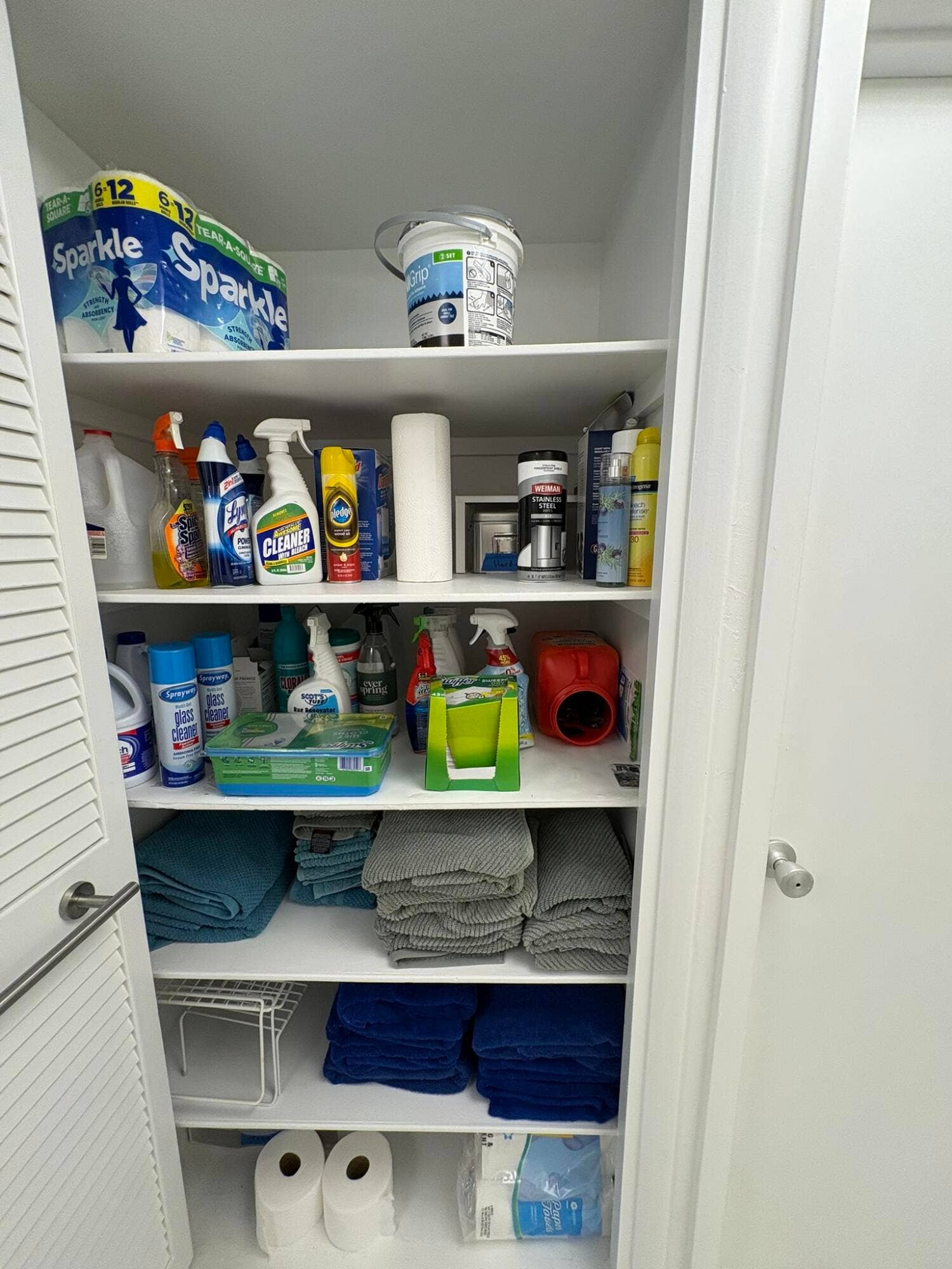 Storage closet featuring six levels of white shelving and louvered double doors