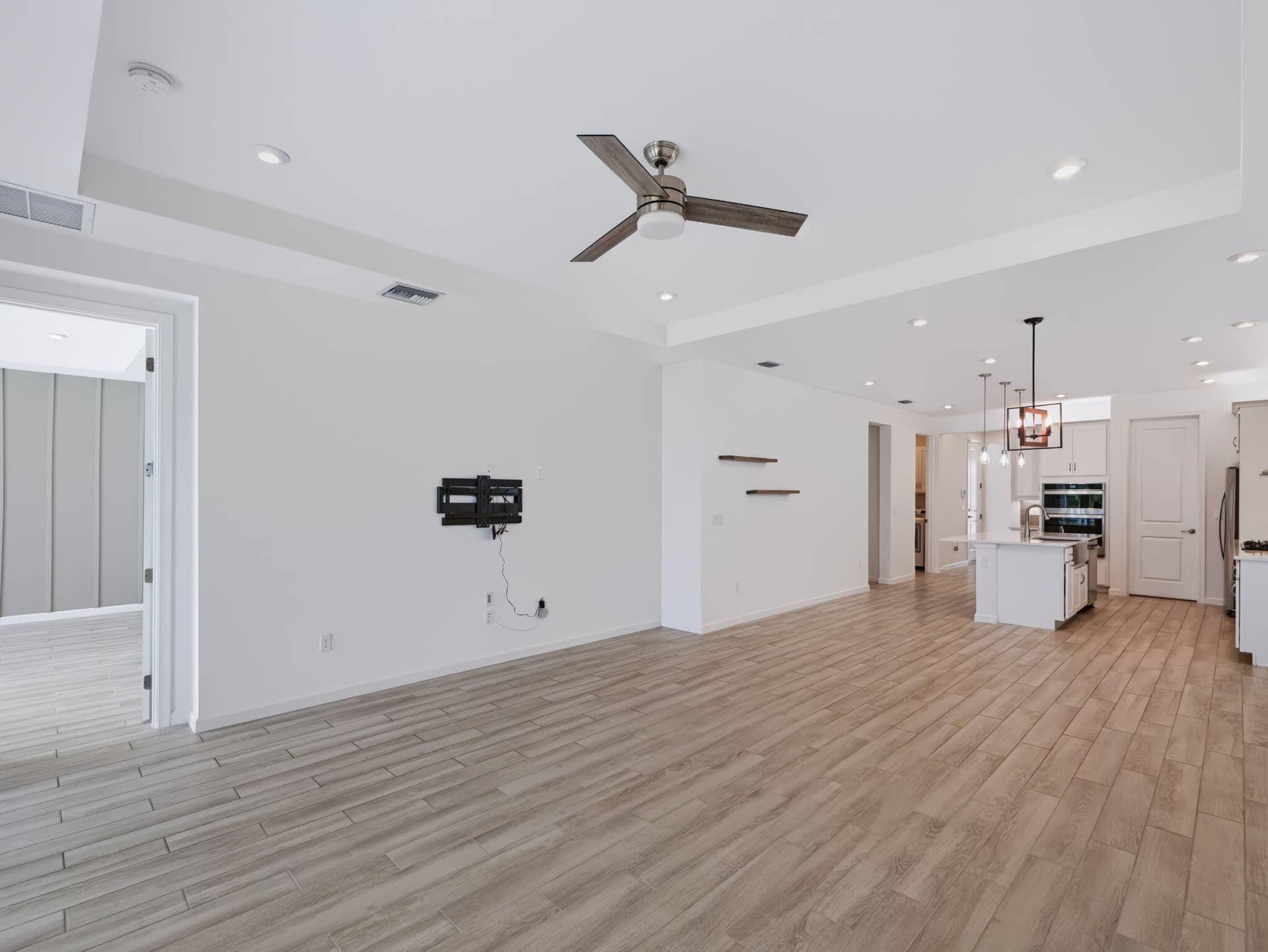12688 SW Eleanor Drive, Port St Lucie, FL 34987 Open-concept interior featuring tray ceilings, recessed lighting, wood-finish tile flooring, a modern three-blade ceiling fan, and built-in wall shelving