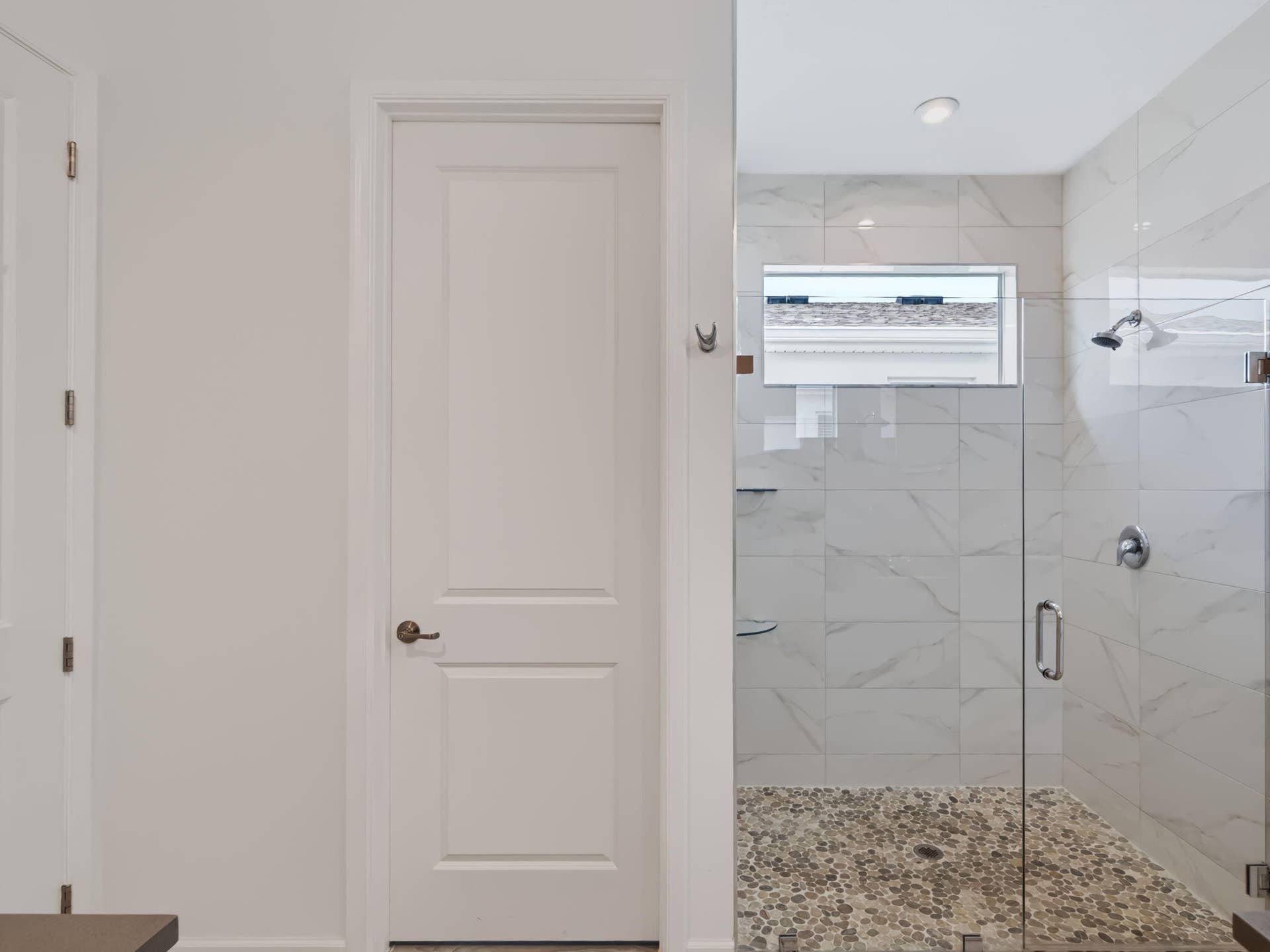 12688 SW Eleanor Drive, Port St Lucie, FL 34987 Walk-in shower featuring large-format tile wall surround, pebble-texture stone flooring, frameless glass enclosure, built-in shelving, and polished chrome fixtures