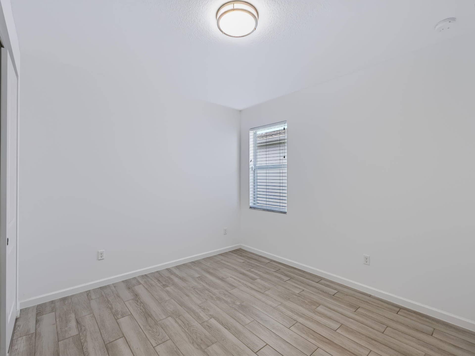 12688 SW Eleanor Drive, Port St Lucie, FL 34987 Interior room featuring wood-finish flooring, a neutral color palette, a single window with horizontal blinds, and a circular flush-mount ceiling light