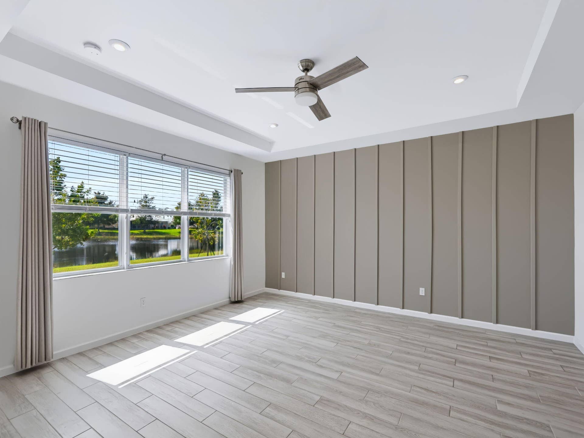 12688 SW Eleanor Drive, Port St Lucie, FL 34987 Tray ceiling with recessed lighting, vertical board-and-batten accent wall, wood-finish flooring, and a central ceiling fan