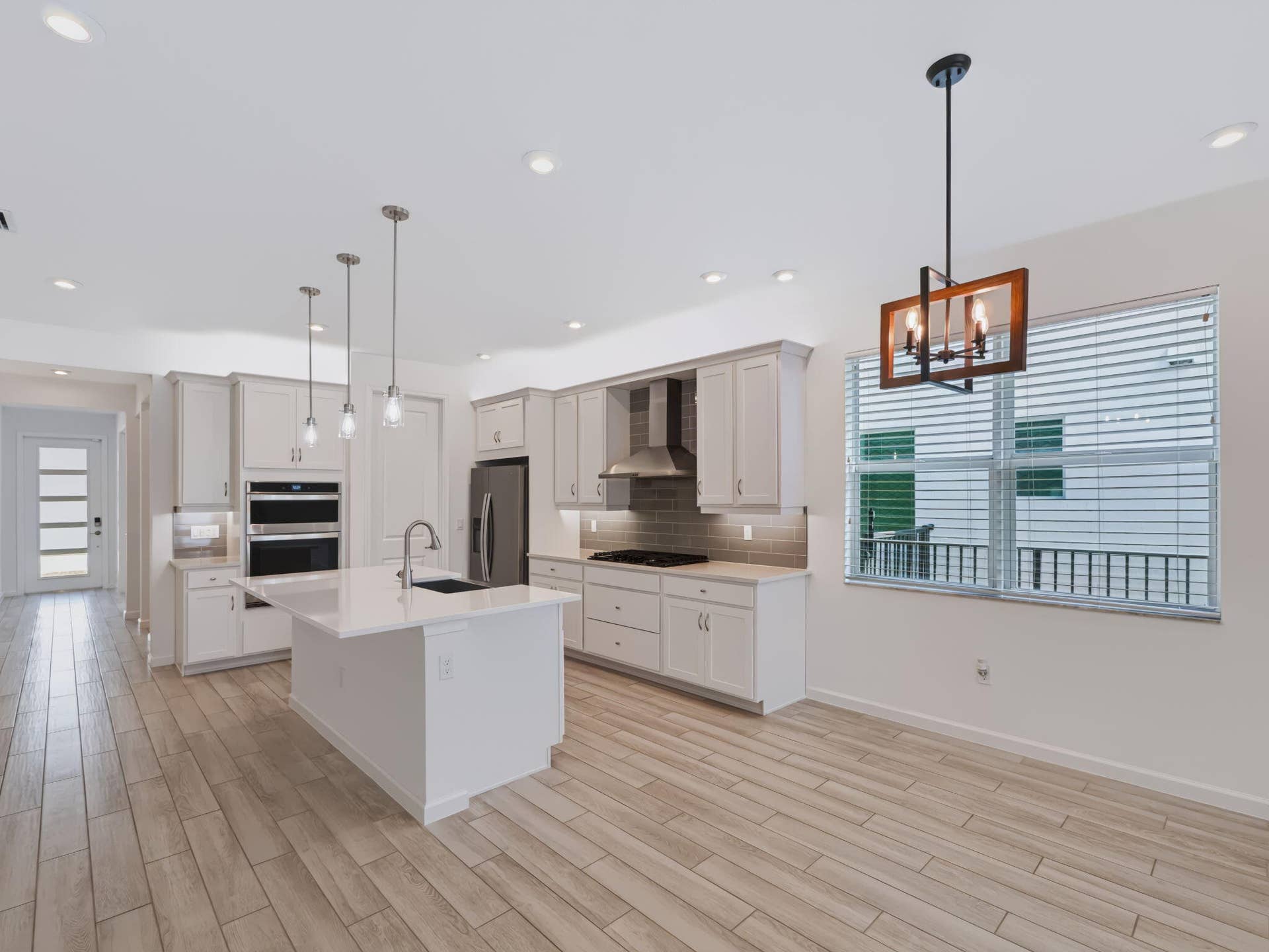 12688 SW Eleanor Drive, Port St Lucie, FL 34987 Kitchen featuring light-toned cabinetry, quartz countertops, a central island with an integrated sink, built-in stainless steel appliances, and wood-finish flooring