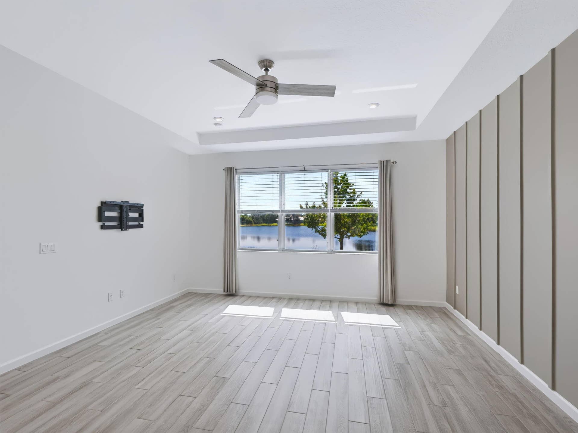 12688 SW Eleanor Drive, Port St Lucie, FL 34987 Tray ceiling with a central brushed-nickel ceiling fan, wood-finish tile flooring, and vertical wall paneling accents