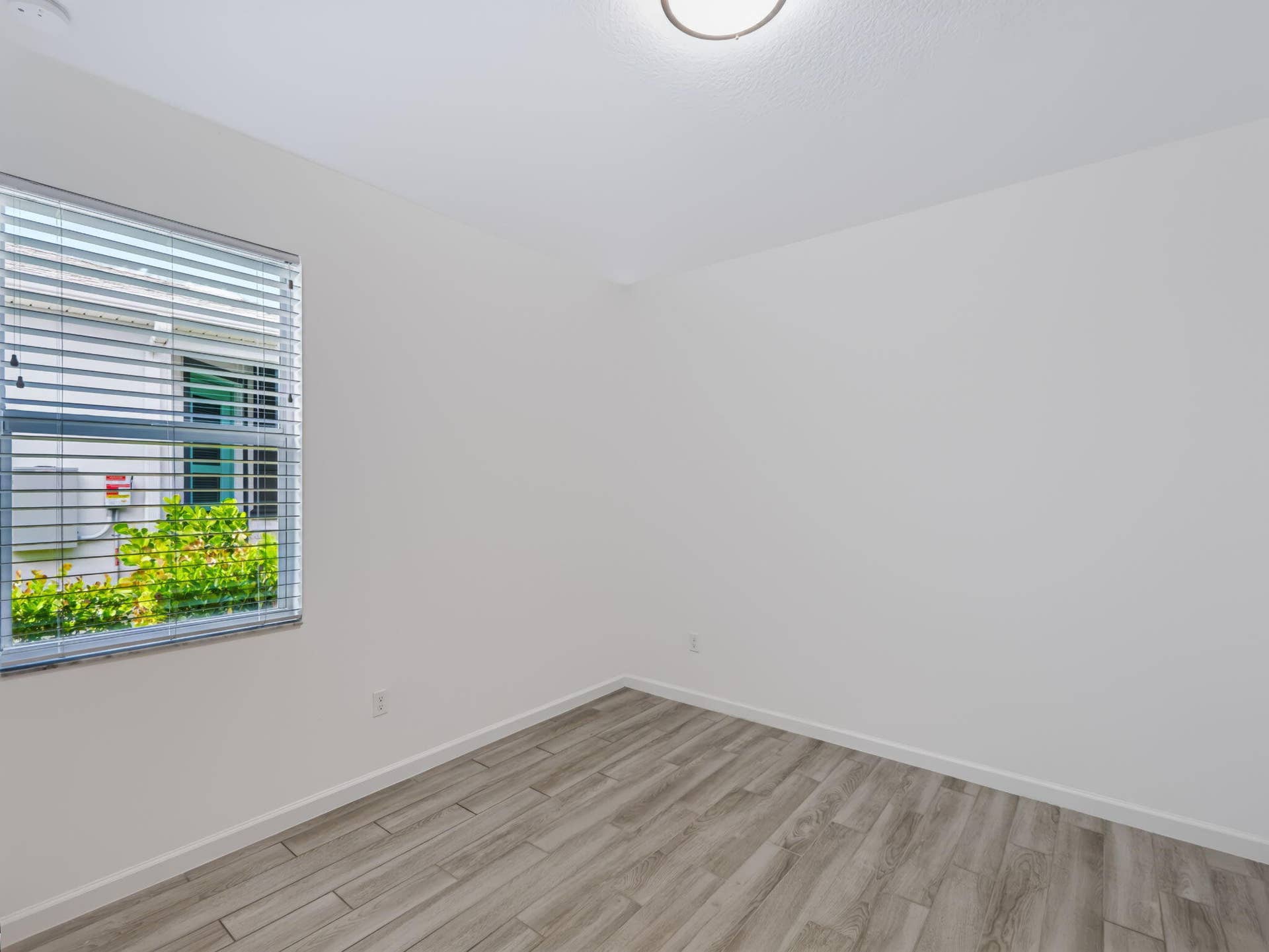 12688 SW Eleanor Drive, Port St Lucie, FL 34987 Neutral-toned interior space featuring wood-finish flooring, white walls, a flush-mount light fixture, and a window equipped with horizontal blinds