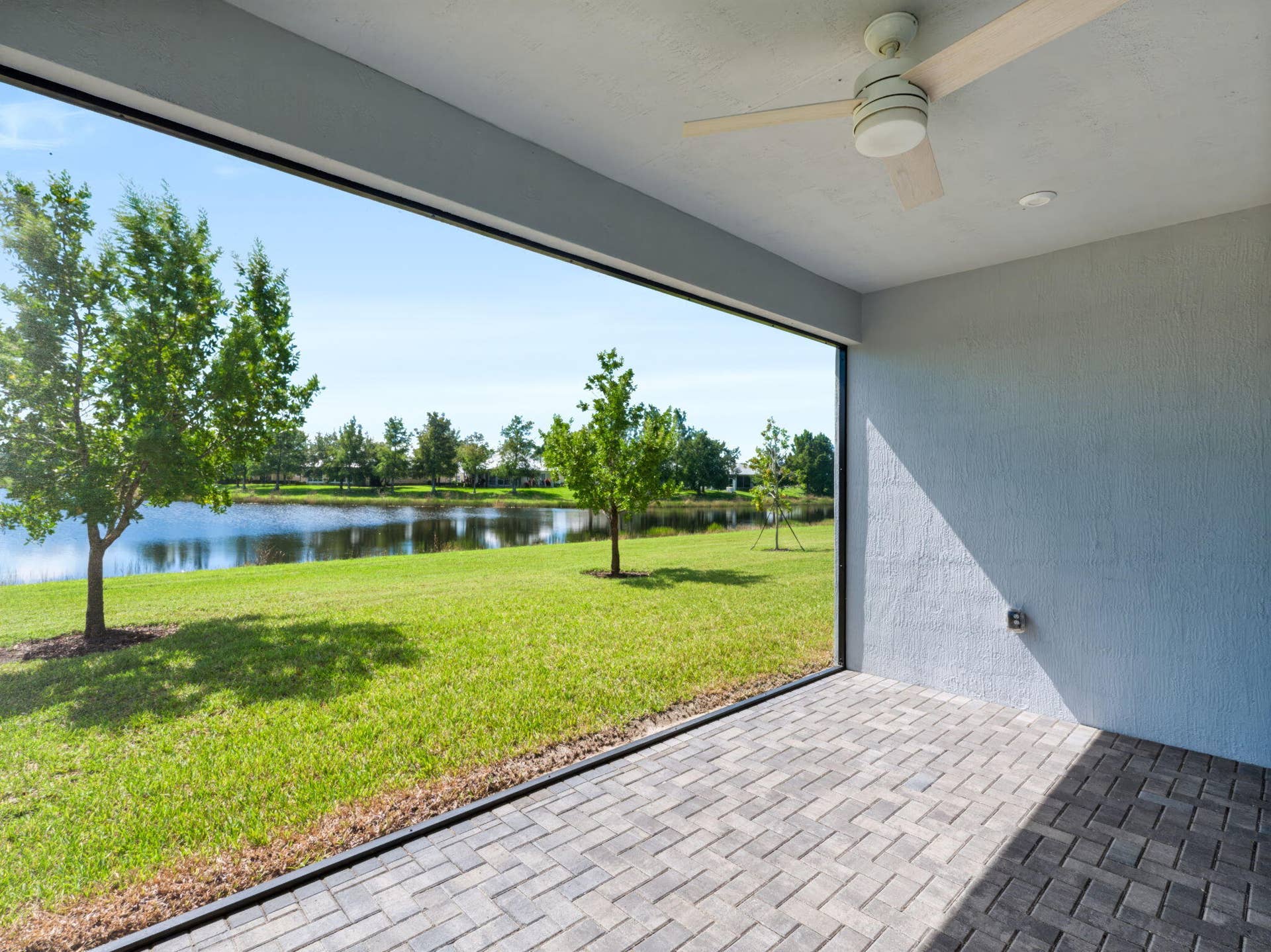 12688 SW Eleanor Drive, Port St Lucie, FL 34987 Covered patio with stone-paver flooring, ceiling fan, and screen enclosure overlooking a manicured lawn and pond