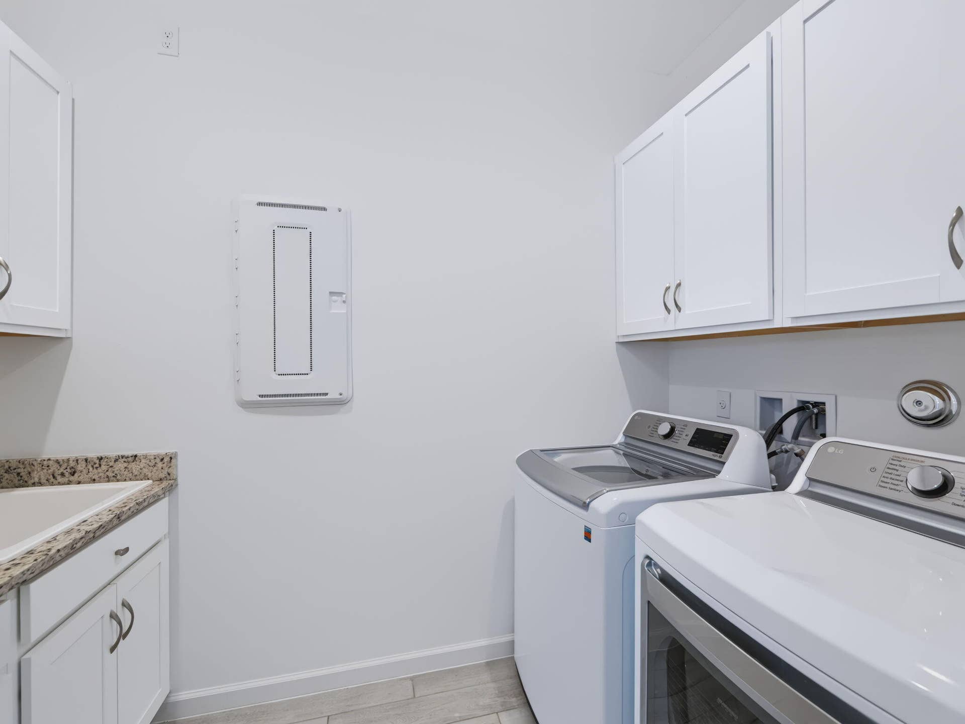 12688 SW Eleanor Drive, Port St Lucie, FL 34987 Laundry room featuring white shaker-style cabinetry, stone-surface countertop with an integrated basin, and neutral tile flooring